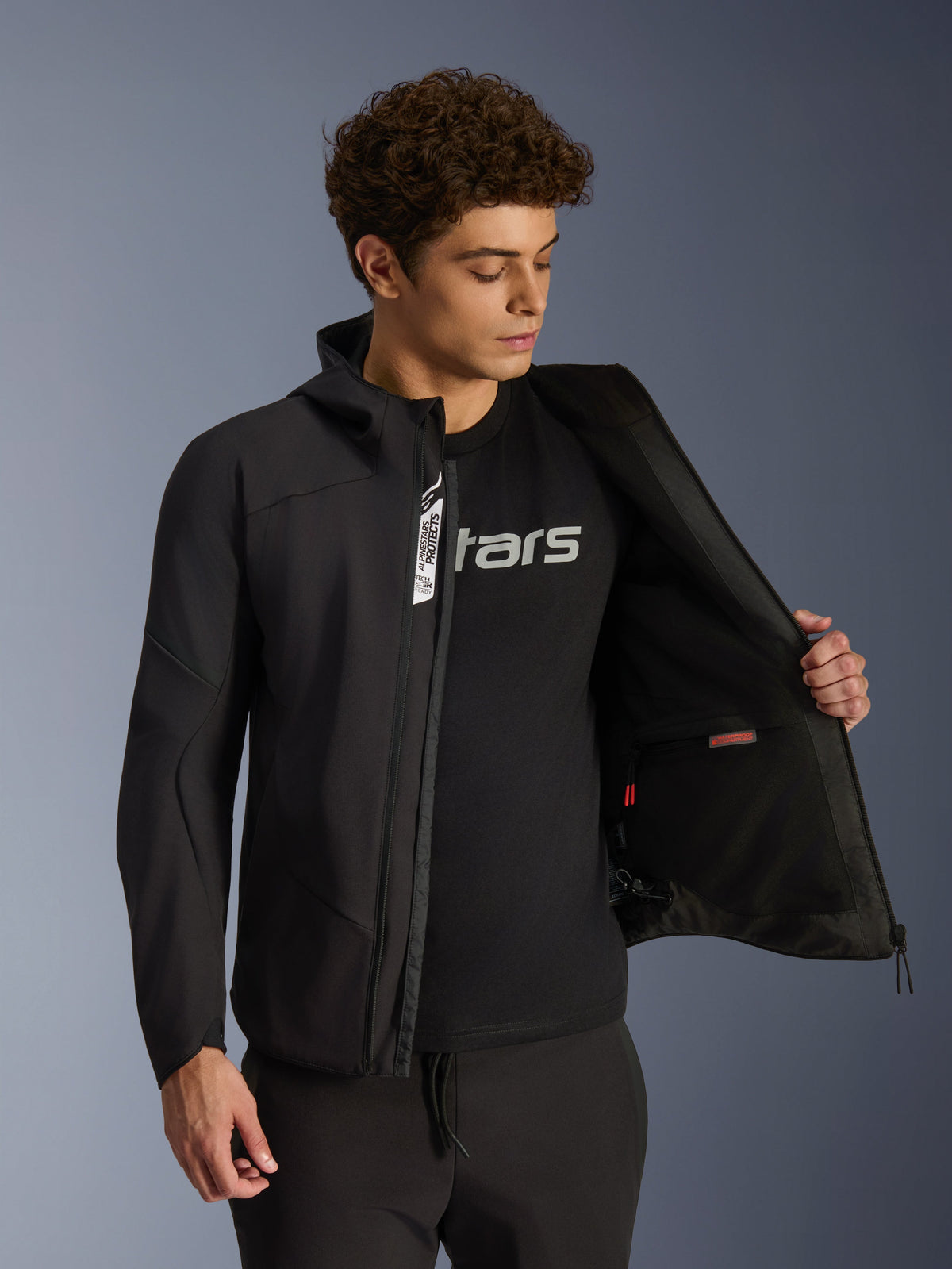 Alpinestars Aeroshell waterdichte jas, zwarte softshell urban herenmotorjas, opengeritst met zichtbare binnenzak.