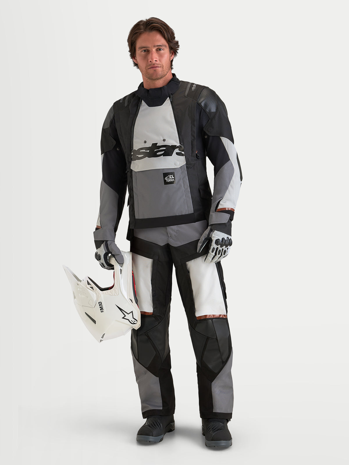 Alpinestars Harok V2 Drystar jas, heren motorjas voor terreinrijden en adventure, donkergrijs, ijsgrijs en zwart, waterdichte textielconstructie met CE-gecertificeerde bescherming, gedragen door een mannelijk model die een witte helm vasthoudt