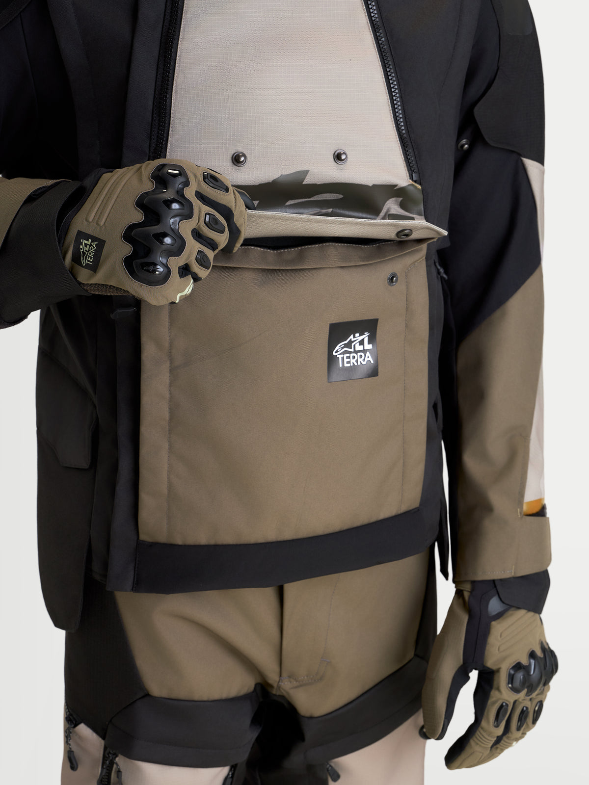 Alpinestars Harok V 2 Drystar Jacke, Adventure-Motorradjacke in Aluminium, Walnussbraun und Schwarz, Detailaufnahme der wasserdichten Kängurutasche mit Alpinestars All Terra Branding und Schutzhandschuhen