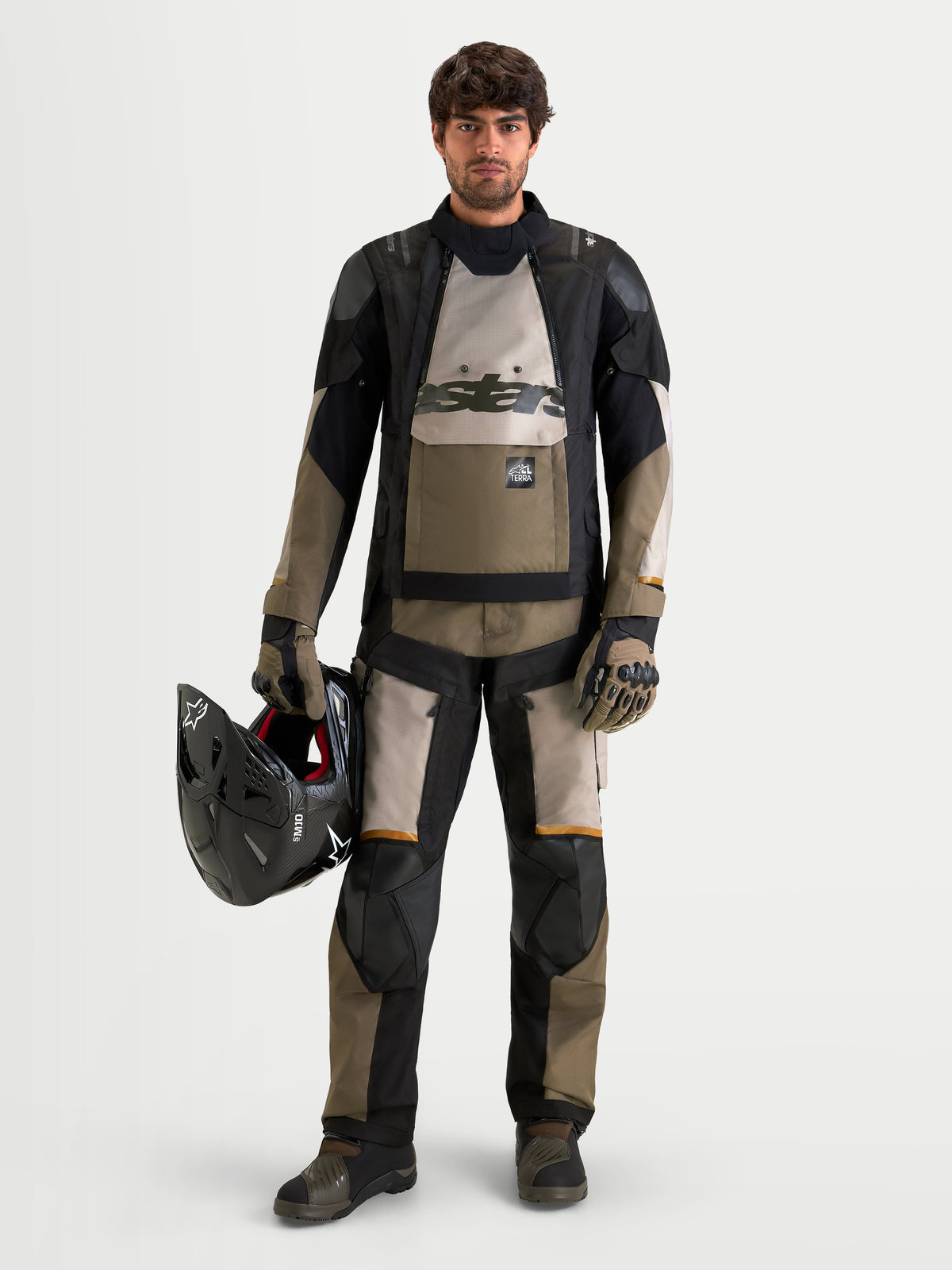 Alpinestars Harok V2 Drystar Jacke, Herren-Adventure-Motorradjacke in Aluminium, Braun und Schwarz, getragen mit passender Adventure-Ausrüstung und Helm in der Hand