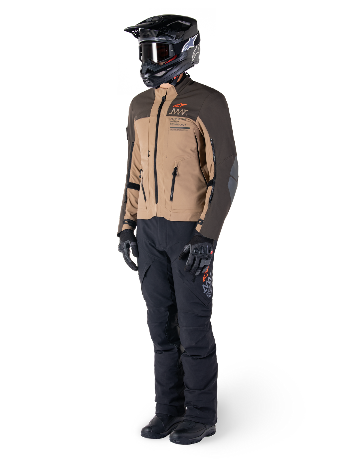 Adventure-motorrijder in volledige uitrusting, Alpinestars AMT-8 Stretch Drystar® XF Jas in donkerbruin en donkerkhaki, gecombineerd met zwarte adventure-broek, zwarte helm, handschoenen en laarzen, voorzien van oranje AMT-branding en technische ventilatieritsen voor touring over lange afstanden