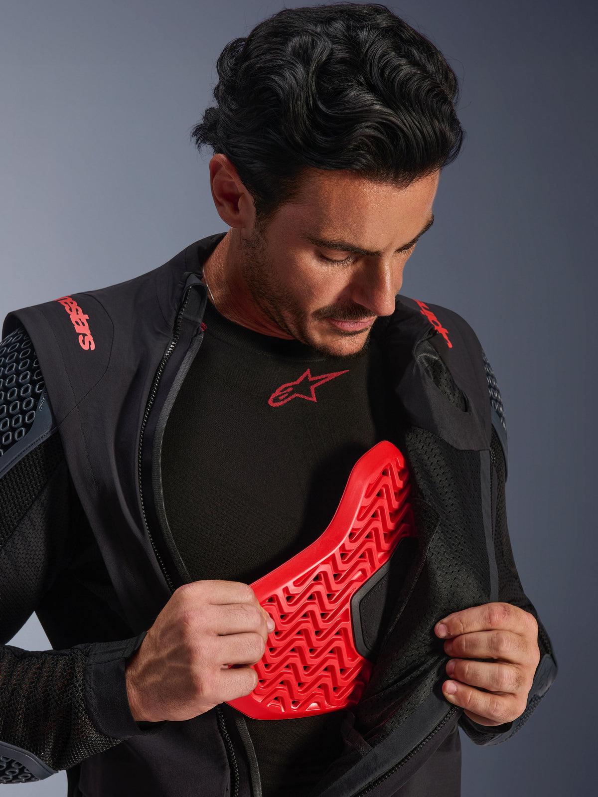 Alpinestars Halo Pro Drystar® XF Gelamineerd Jack in Black Dark Shadow, gedragen door een model en opengeritst om een rode Nucleon Flex Pro borstbeschermer te onthullen, technische motorjas met geïntegreerde bescherming, adventure motorkleding.