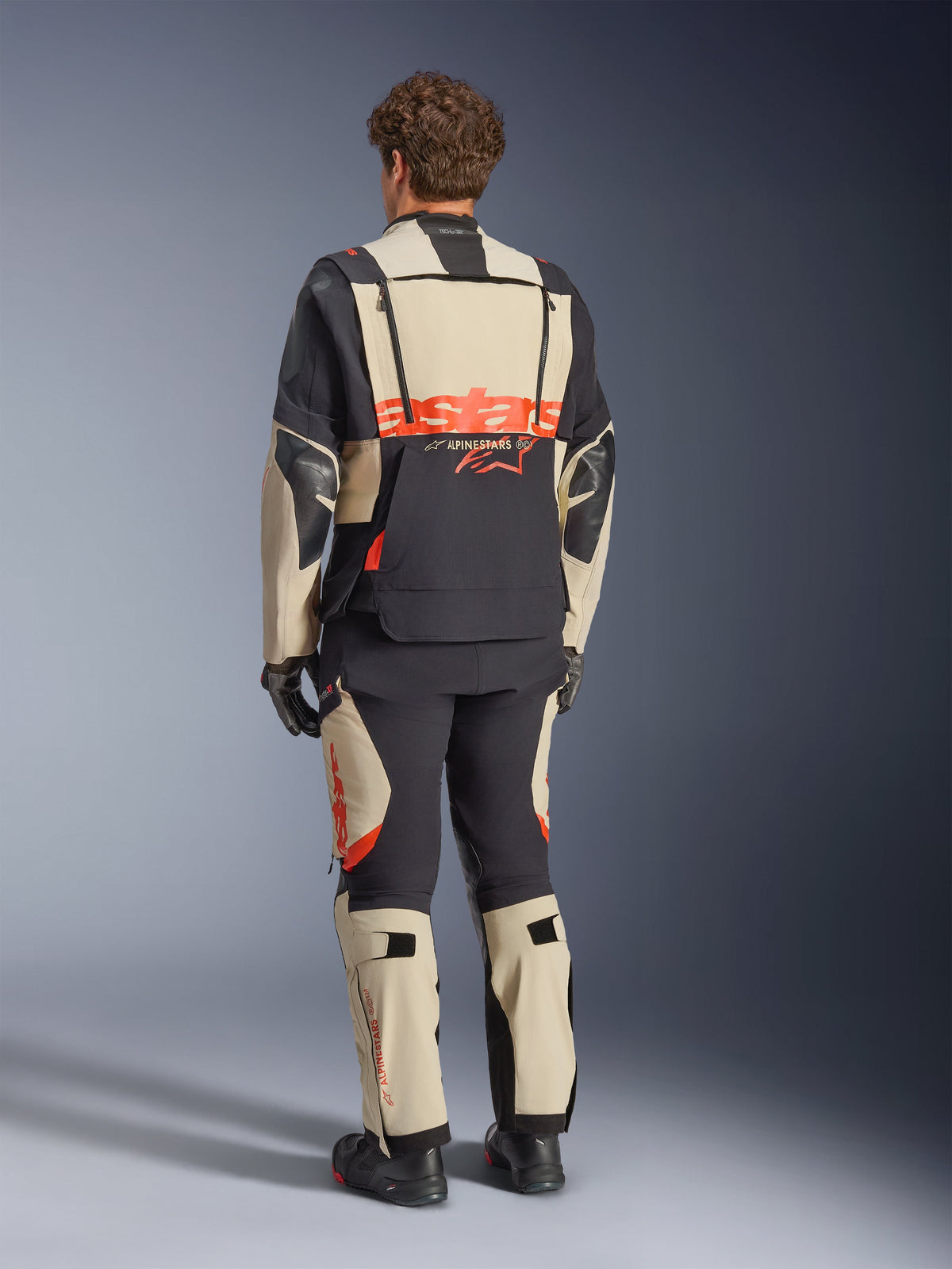 Alpinestars Halo Pro Drystar® XF Laminated Jacket, Mastic Black, back view, adventure motorcycle jacket with large orange 'astars' branding across the rear, worn with matching technical pants and boots, modular design for versatile terrain