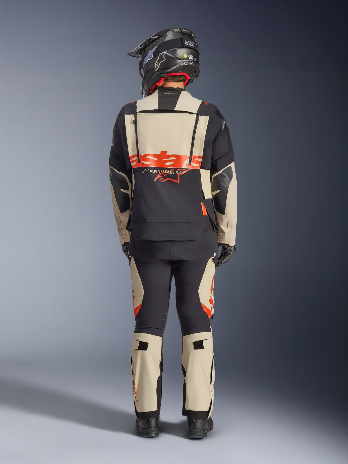 Alpinestars Halo Pro Drystar® XF Laminated Jacket, Adventure Motorcycle Jacket, Mastic Black, back view of a rider wearing matching pants and a black helmet, featuring bold orange Alpinestars branding and modular ventilation panels for versatile adventure riding.