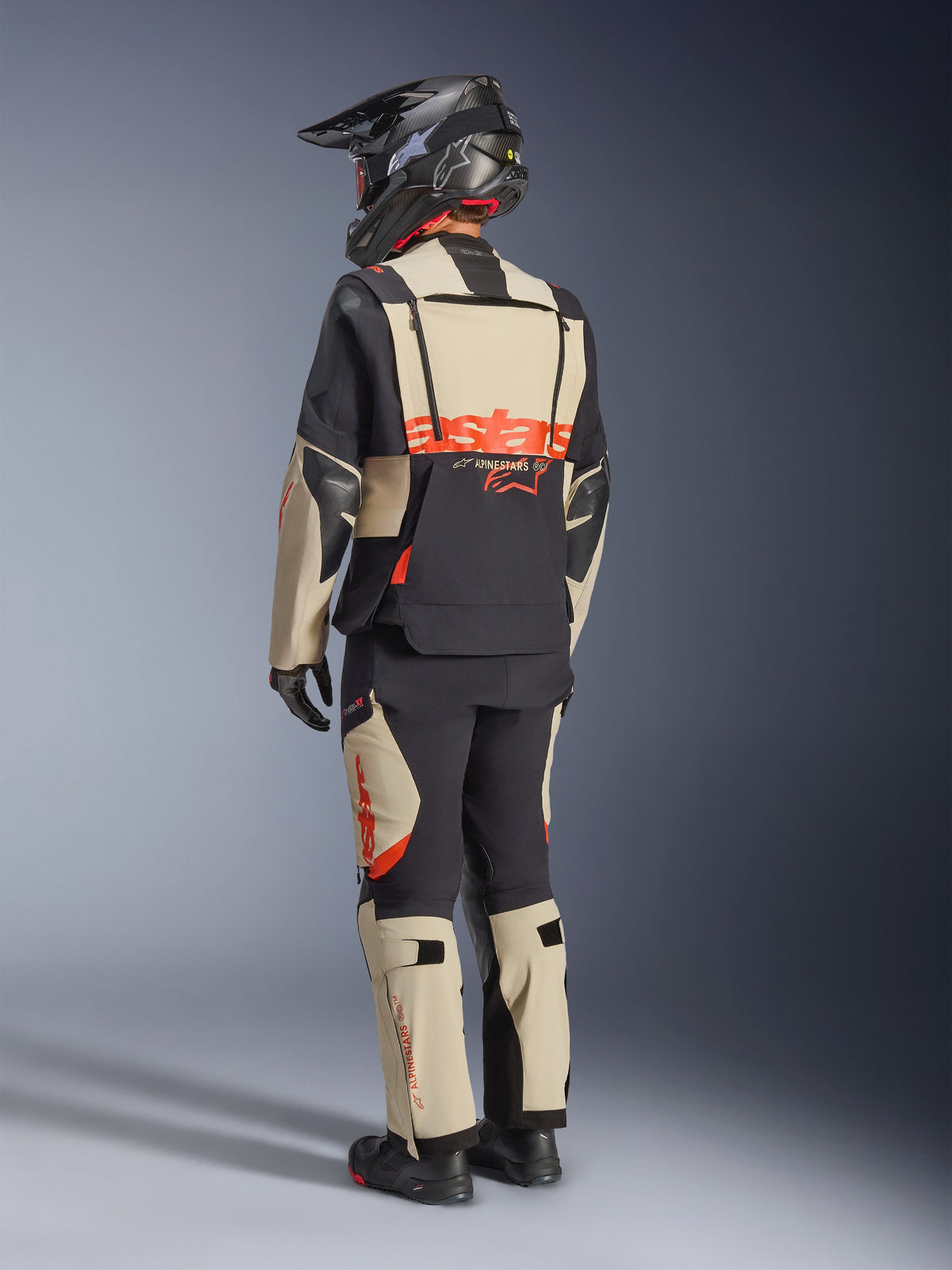 Alpinestars Halo Pro Drystar® XF Laminated Jacket, Mastic Black, rear view of a rider wearing the full adventure motorcycle suit with matching pants, black adventure helmet, and boots, featuring a bold red Alpinestars logo across the back.