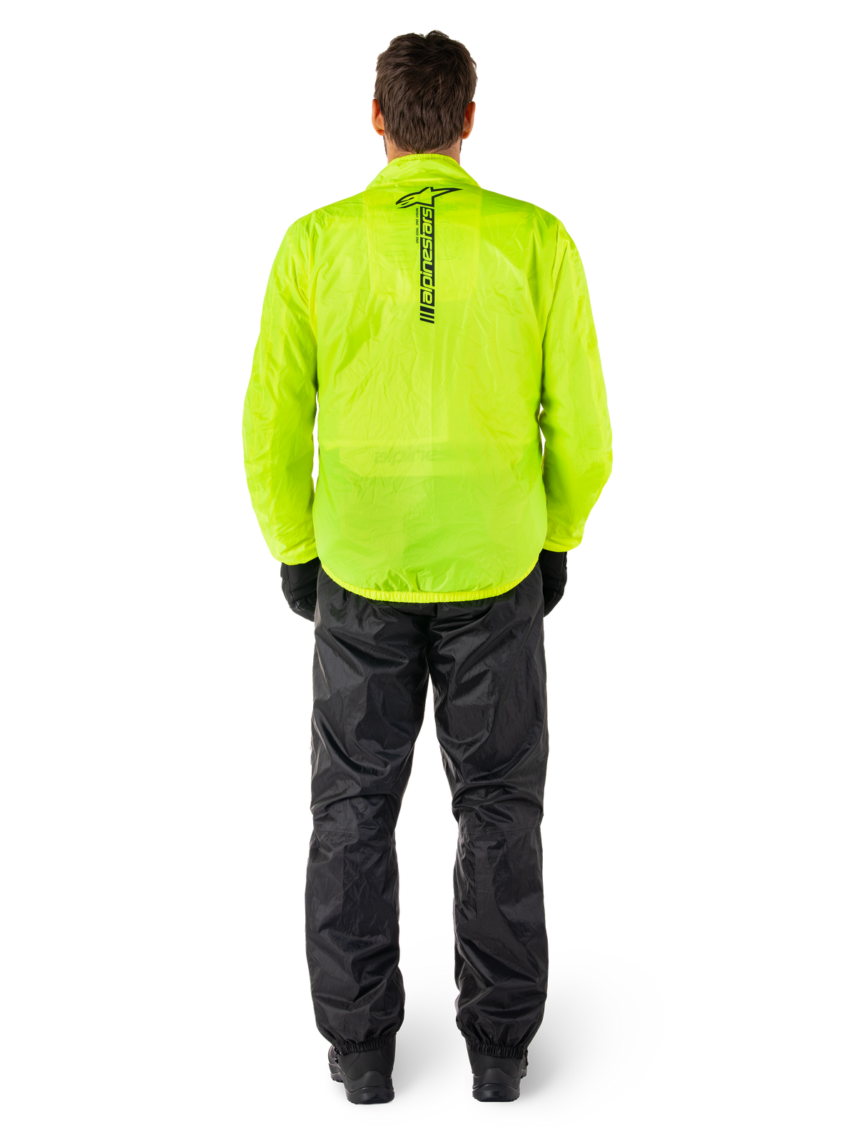 Alpinestars Hurricane Rain V2 jas en broek, waterdicht motorregenpak, fel fluorgele jas met verticaal zwart logo op de rug, zwarte broek, lichtgewicht textielmateriaal ontworpen voor bescherming in natte weersomstandigheden, persoon van achteren gezien