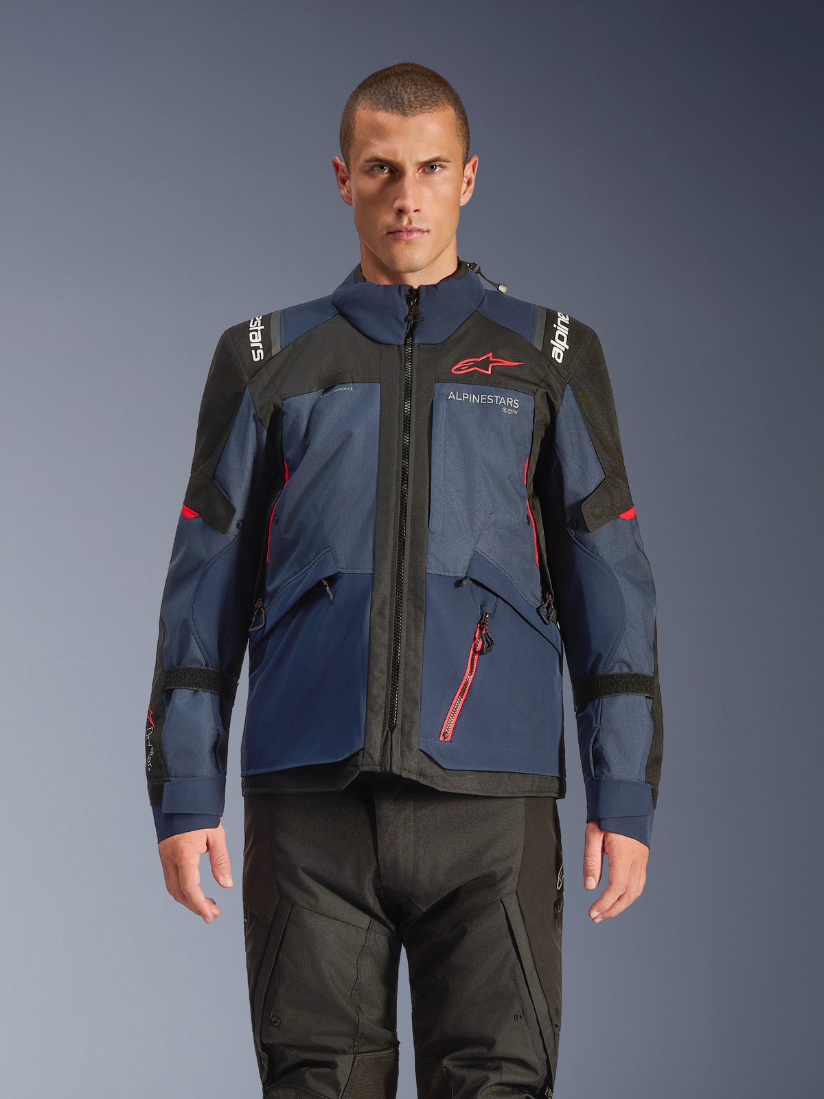 Veste Alpinestars Andes V4 Drystar®, veste de moto d'aventure, Night Navy et Mood Indigo avec empiècements noirs, portée par un mannequin avec un pantalon de moto noir, logo Alpinestars rouge sur la poitrine et détails de fermeture éclair rouges, construction textile durable pour le touring toutes saisons