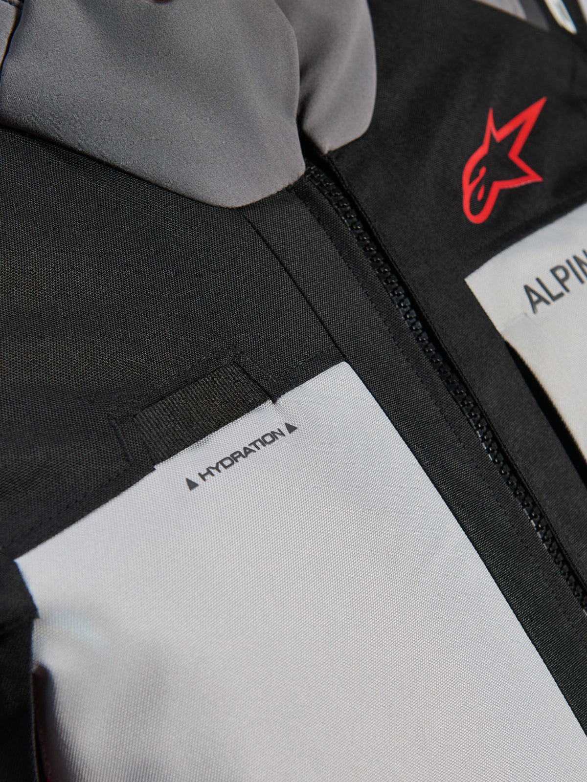 Veste Alpinestars Andes V4 Drystar®, gros plan sur la poitrine, panneaux gris foncé et gris glace avec renforts en textile noir, logo Alpinestars rouge et boucle pour tuyau d'hydratation avec étiquette 'HYDRATION'