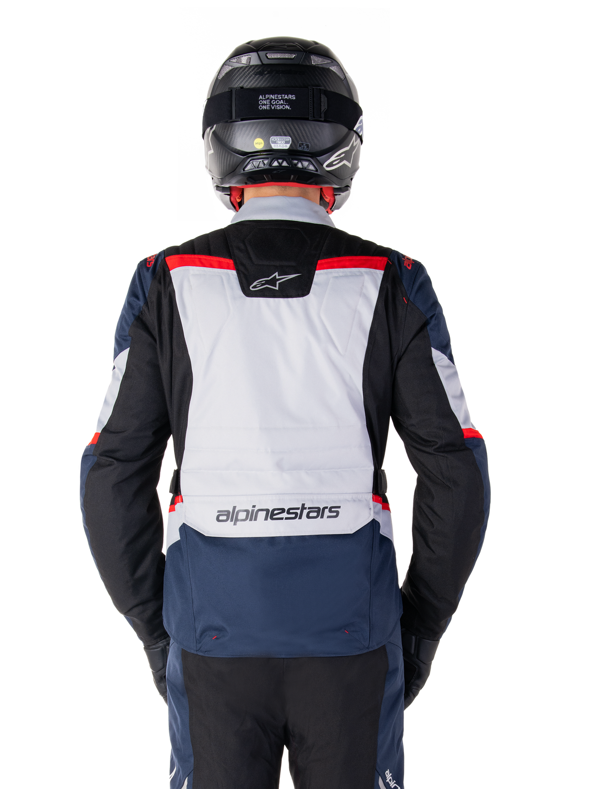 Veste imperméable Alpinestars ST-1, bleu foncé, noir et rouge vif, vue arrière montrant le panneau dorsal gris clair et le logo, veste de moto adventure touring portée avec un casque et des gants noirs, design épuré pour rouler par tous les temps