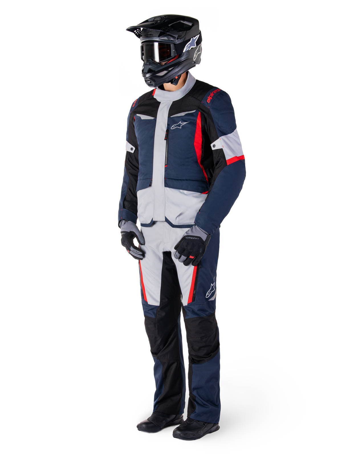 Veste Alpinestars ST-1 Waterproof, veste de tourisme d'aventure, bleu foncé, noir et rouge vif, portée par un motard avec pantalon assorti, casque d'aventure noir, gants et bottes, avec empiècements gris et touches de rouge, design épuré inspiré de l'aventure avec logos Alpinestars