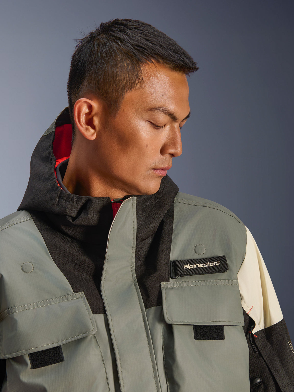 Veste Alpinestars Mospher WP, parka de moto imperméable, Fur Gray Black Ice, gros plan d'un mannequin portant une veste à capuche avec poches utilitaires, languette de logo Alpinestars noire et design tactique avec doublure intérieure rouge
