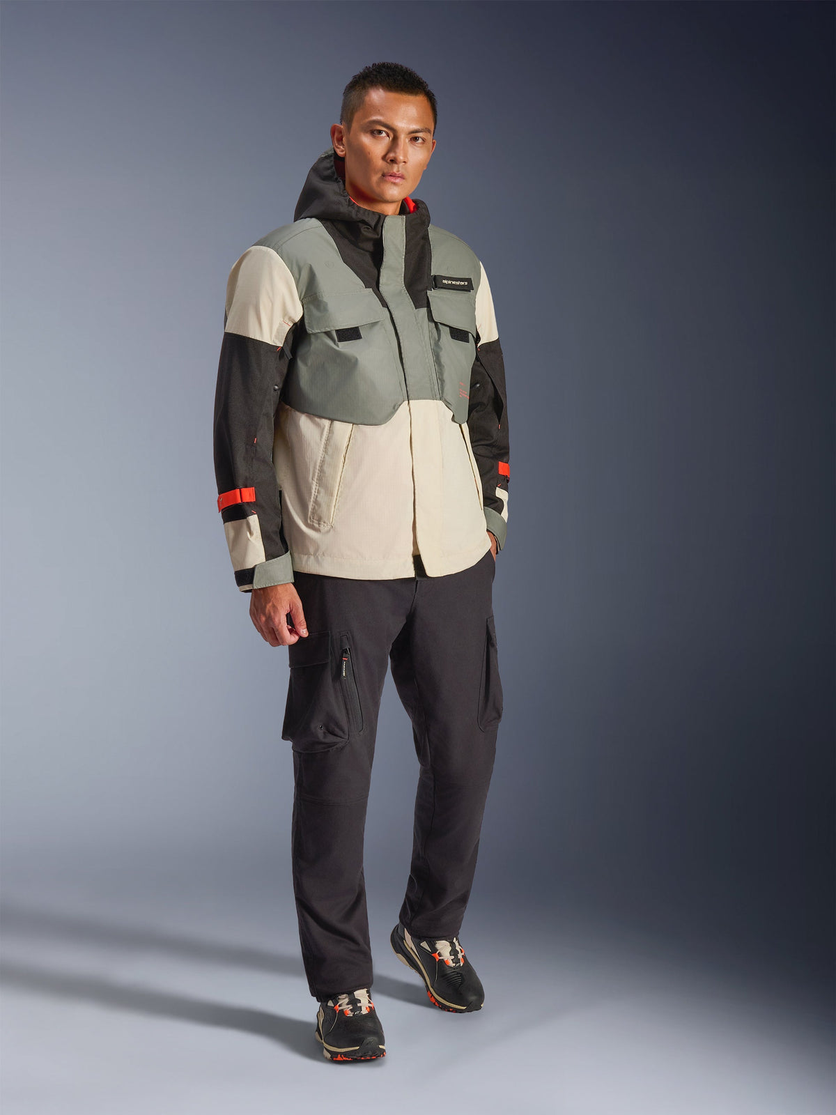 Veste imperméable Alpinestars Mospher en Fur Gray Black Ice, parka de moto technique multicolore avec panneaux gris, noirs et blanc cassé et touches de rouge, design fonctionnel avec grandes poches et capuche, portée avec un pantalon cargo gris foncé et des baskets noires, équipement de moto urbain contemporain