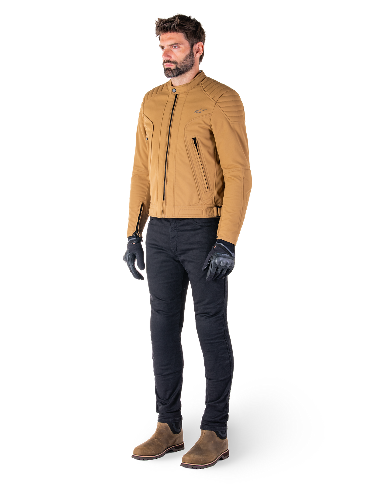 Mannelijke motorrijder draagt de Alpinestars Clayton WR Jas in Utility Brown Light Gold, een urban contemporary motorjas met gewatteerde schouderdetails, gecombineerd met een zwarte broek, zwarte handschoenen en bruine laarzen