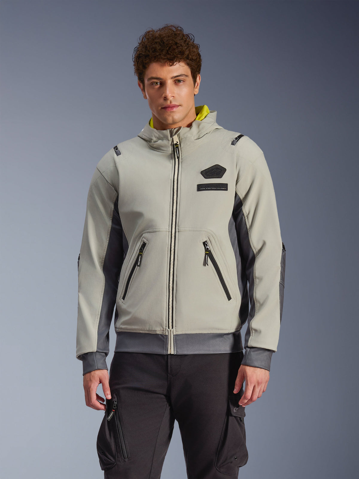 Alpinestars Moblast wasserdichte Jacke, hell- und dunkelgrauer urbaner Motorrad-Hoodie mit gelbem Kapuzenfutter, Fronttaschen und schwarzen Reißverschlüssen, kombiniert mit einer schwarzen Cargohose, modernes sportliches Design