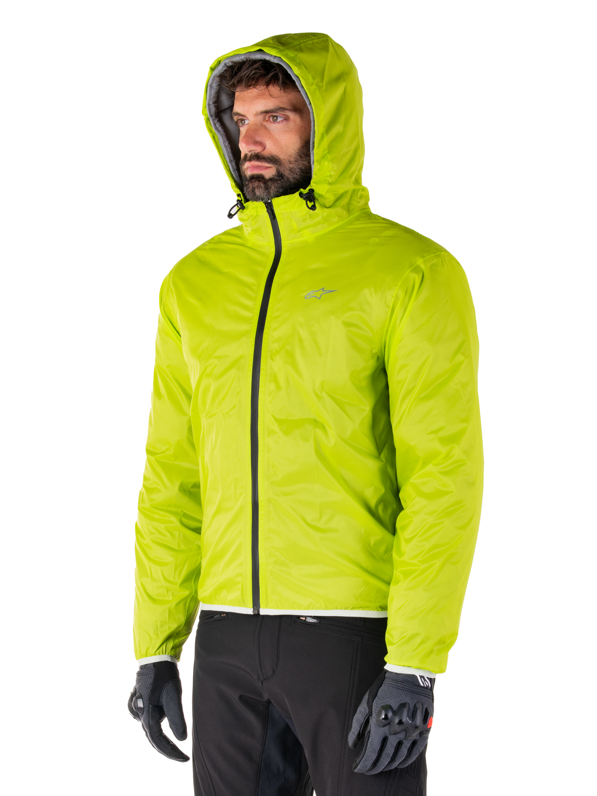 Alpinestars Mohobbs Waterproof Jacket, Lime Punch opvouwbare regenvoering, fel neongroene jas met capuchon gedragen met zwarte broek en grijze handschoenen, op urban streetwear geïnspireerde motorkleding
