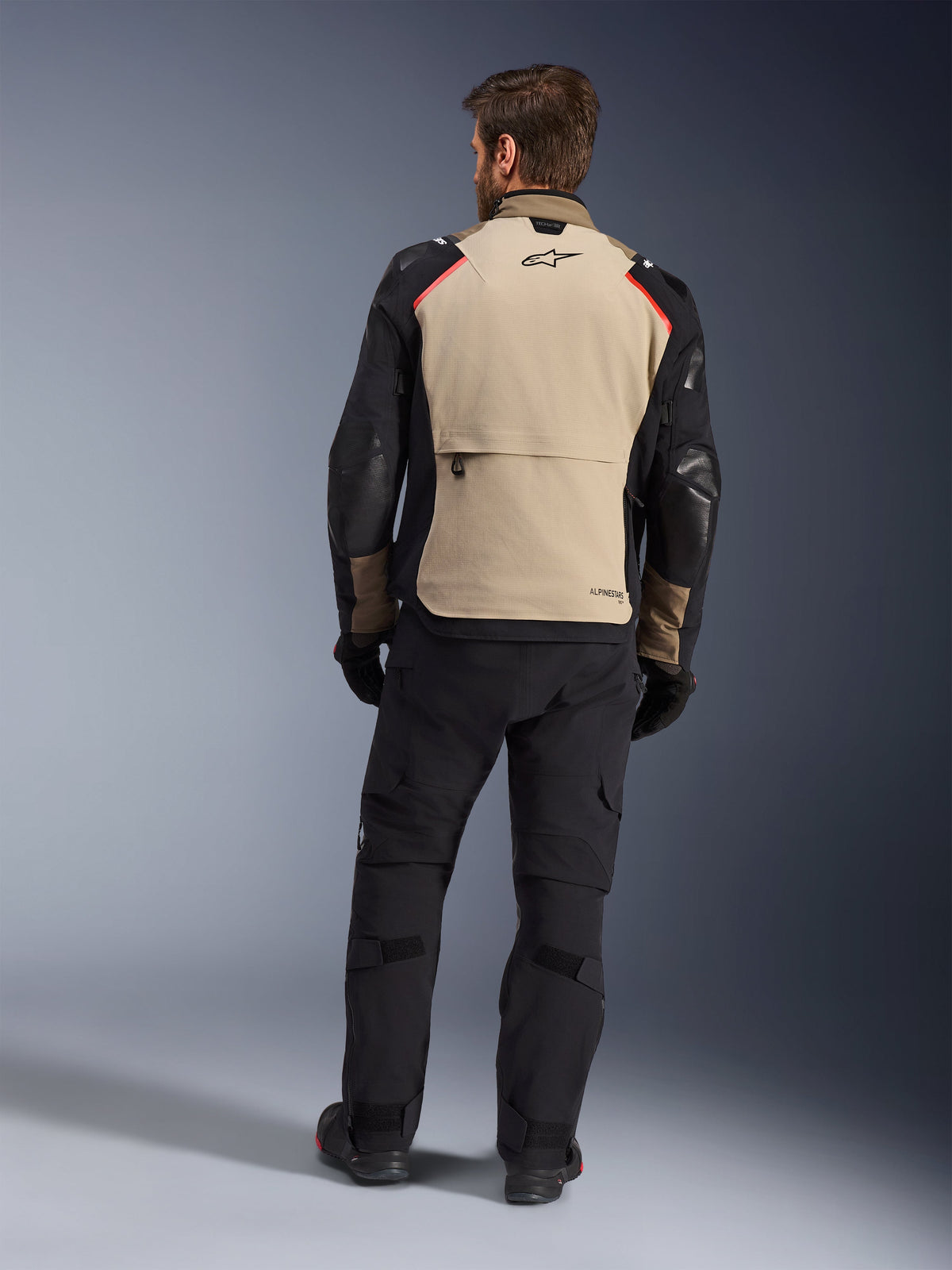 Alpinestars Andes Pro Drystar® XF Jacket, Walnut Aluminum, achteraanzicht, adventure motorjas met zwarte mouwen en rode schouderaccenten, gedragen met zwarte motorbroek en handschoenen