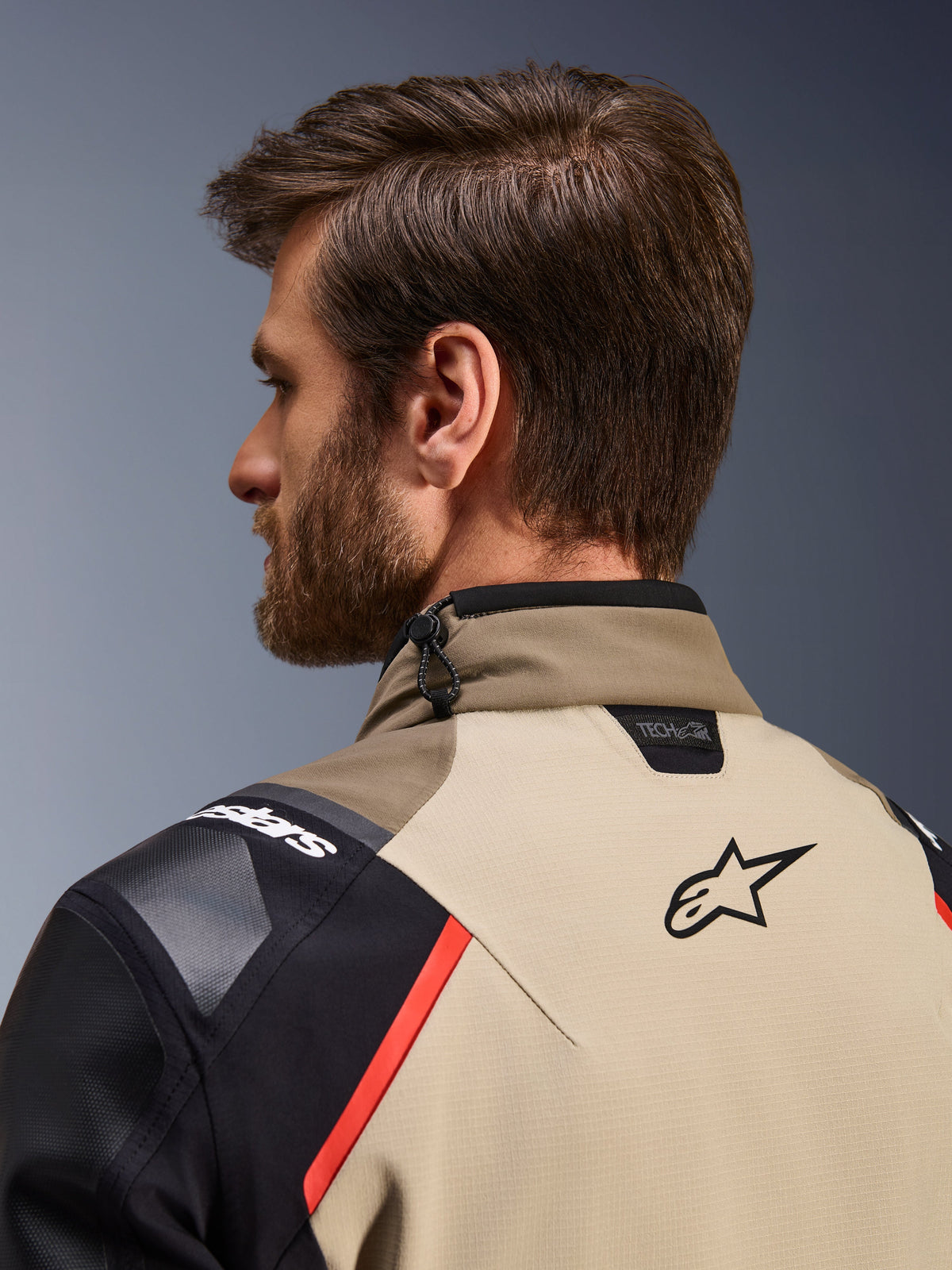 Alpinestars Andes Pro Drystar® XF Jas in Walnut Aluminum, close-up achteraanzicht van de kraag en bovenste schouders, voorzien van het Alpinestars-logo, Tech-Air compatibiliteitsbranding, rode accenten en een schokkoord-verstelsysteem bij de nek.