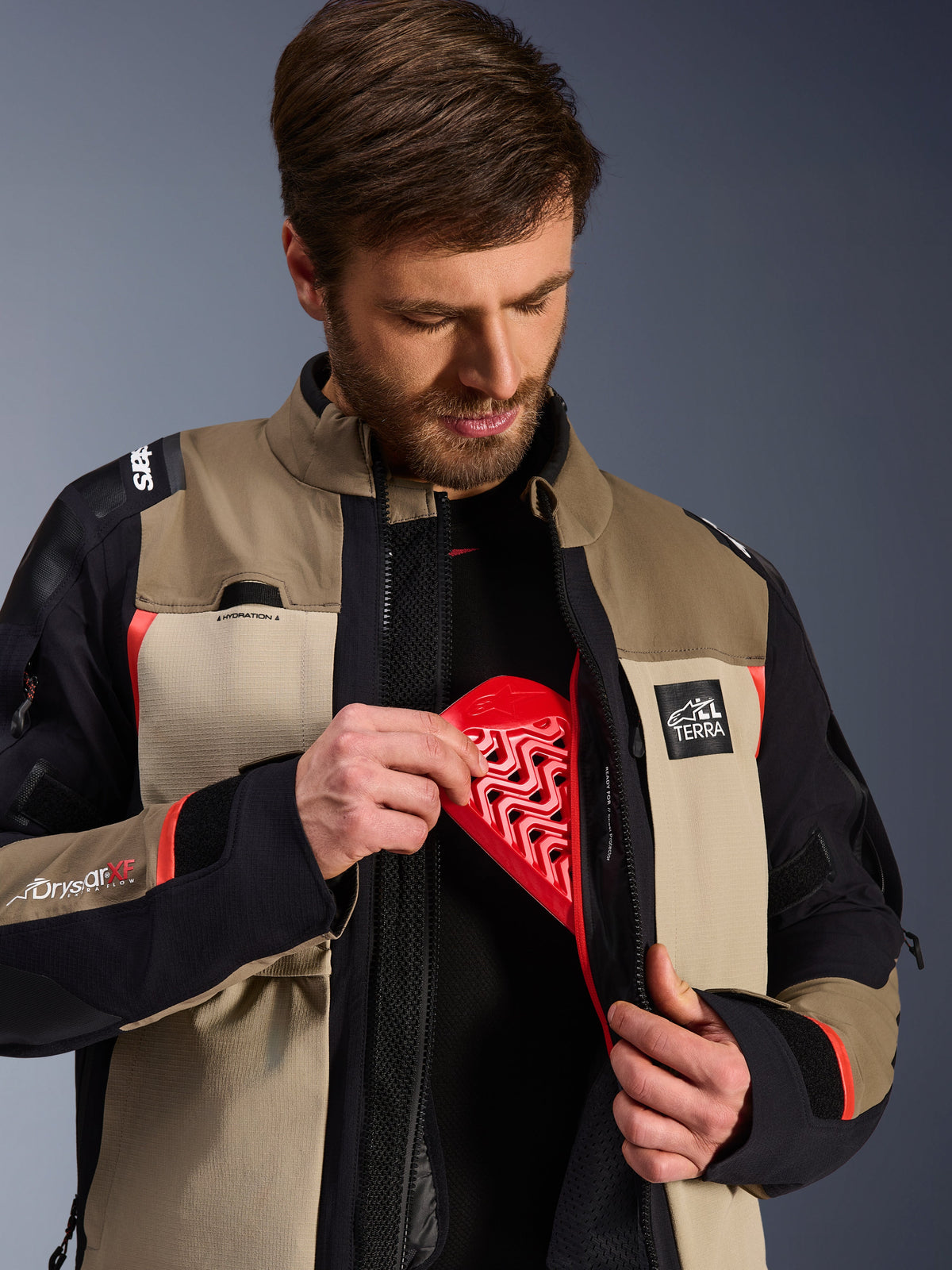 Alpinestars Andes Pro Drystar® XF Jas in Walnut Aluminum, model toont de rode Nucleon borstprotector in de binnenzak, adventure motorjas met ALL TERRA branding en Drystar XF-logo's