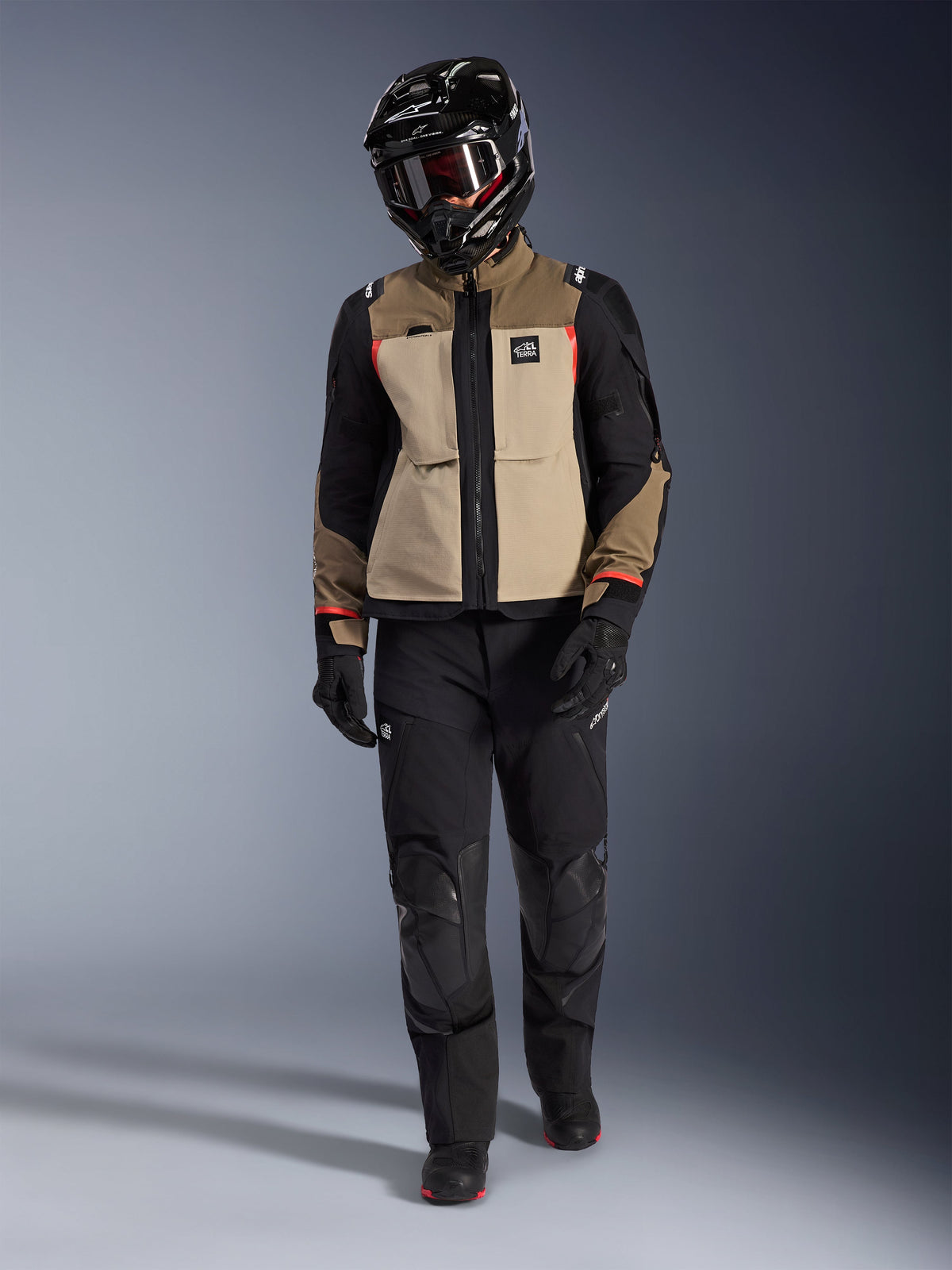 Alpinestars Andes Pro Drystar® XF Jacket in Walnut Aluminum, gedragen met zwarte adventure-broek, zwarte handschoenen en een zwarte integraalhelm met crossbril, voorzien van rode accenten en All Terra-branding, professionele adventure touring-set