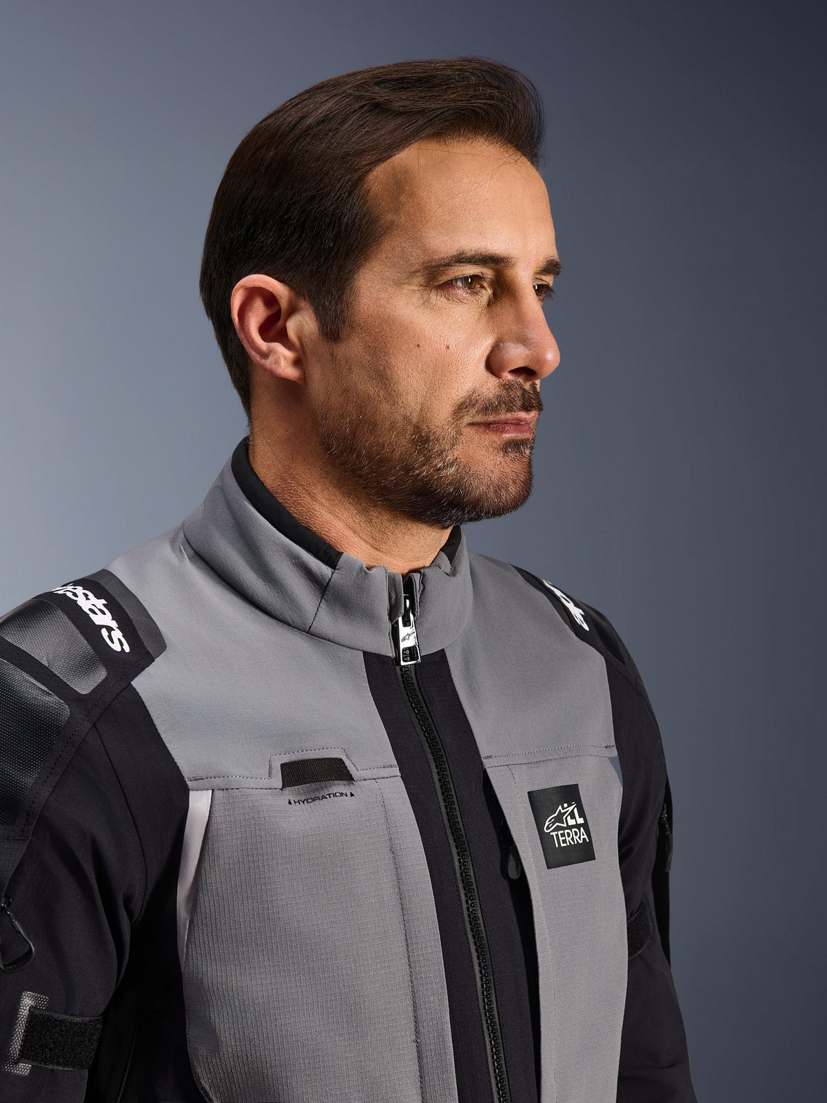 Veste Alpinestars Andes Pro Drystar® XF, veste de moto d'aventure, gris foncé et noir, gros plan sur le buste et le col, présentant le marquage Terra et le détail du passage pour tube d'hydratation, portée par un homme en studio