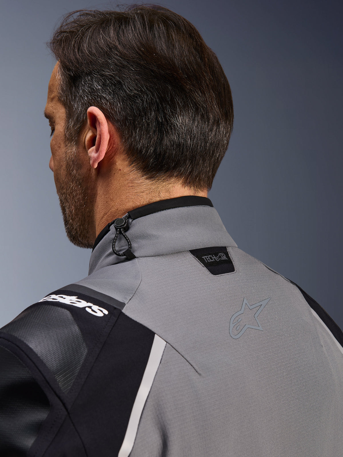 Veste Alpinestars Andes Pro Drystar® XF, gris foncé et noir, gros plan sur le col arrière et le haut de l'épaule, montrant le logo Tech-Air® Ready, le réglage par cordon de serrage et le logo étoile Alpinestars ton sur ton sur le textile technique.