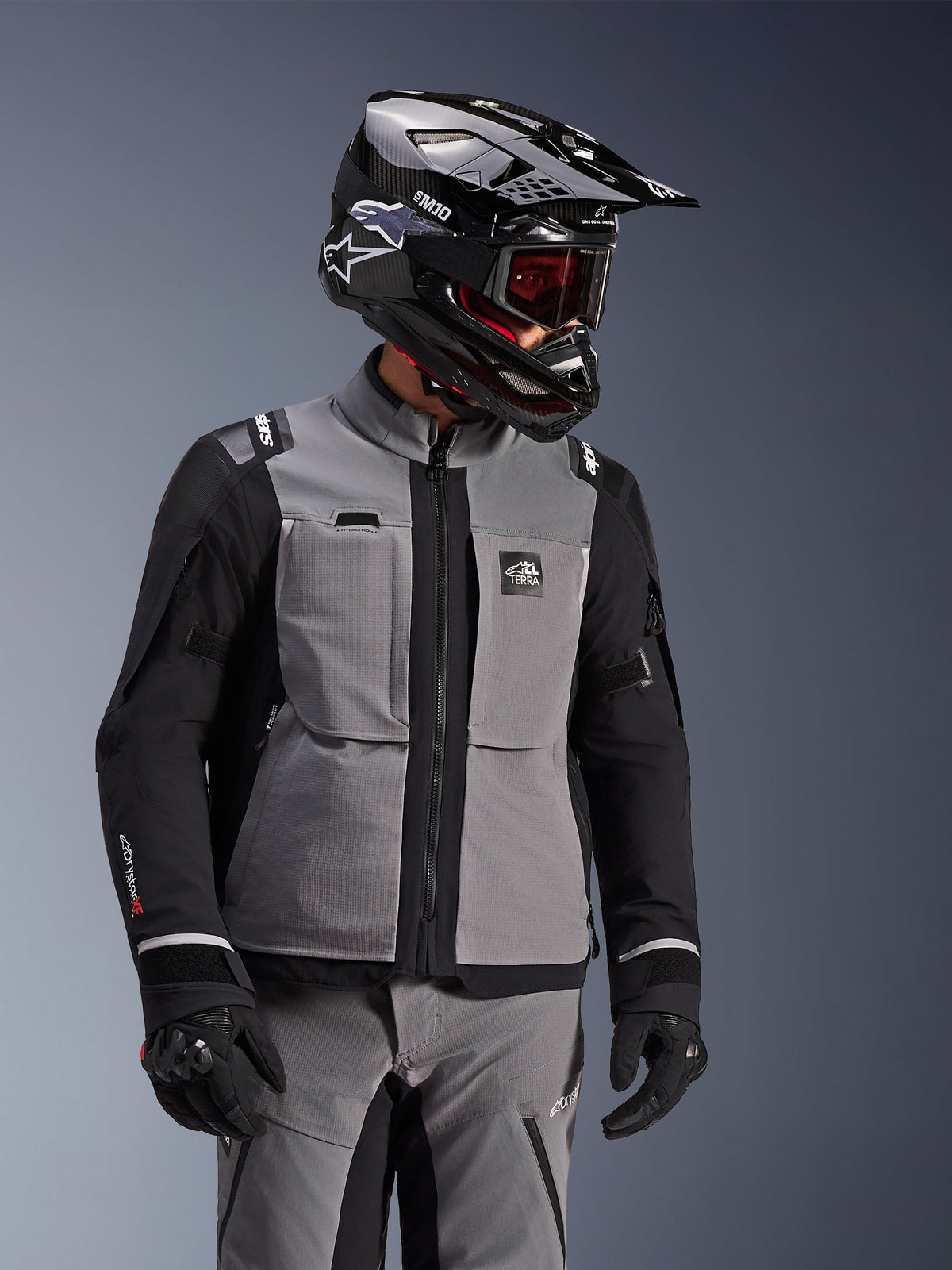 Veste Alpinestars Andes Pro Drystar® XF, gris foncé et noir, veste de moto d'aventure portée avec un casque SM10 noir et un équipement de conduite assorti, conception textile à 3 couches avec fermeture éclair centrale et poches de poitrine, design articulé pour le touring toutes saisons
