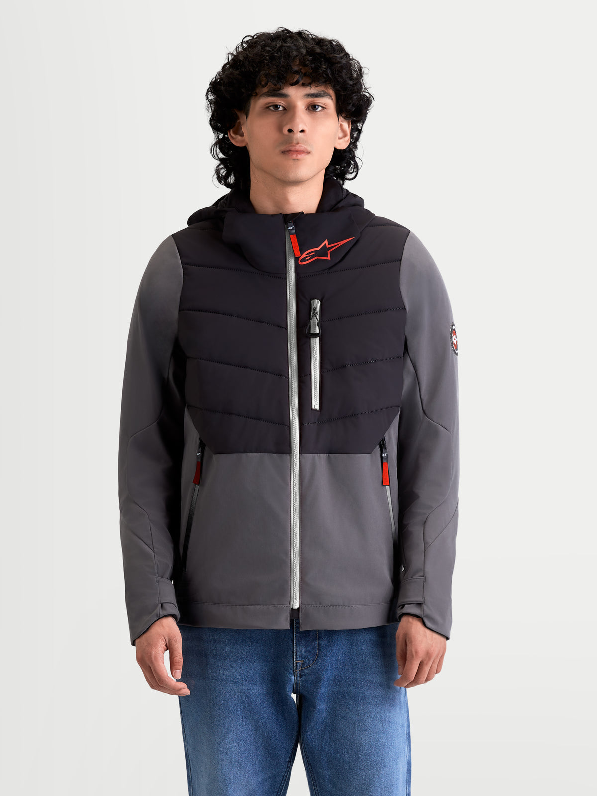 Alpinestars Therma-Tech waterdichte jas, heren motorjas voor stedelijk gebruik in zwart en donkergrijs, vooraanzicht op model met jeans, met sonic-welded donsconstructie, waterdicht membraan en geïntegreerde capuchon
