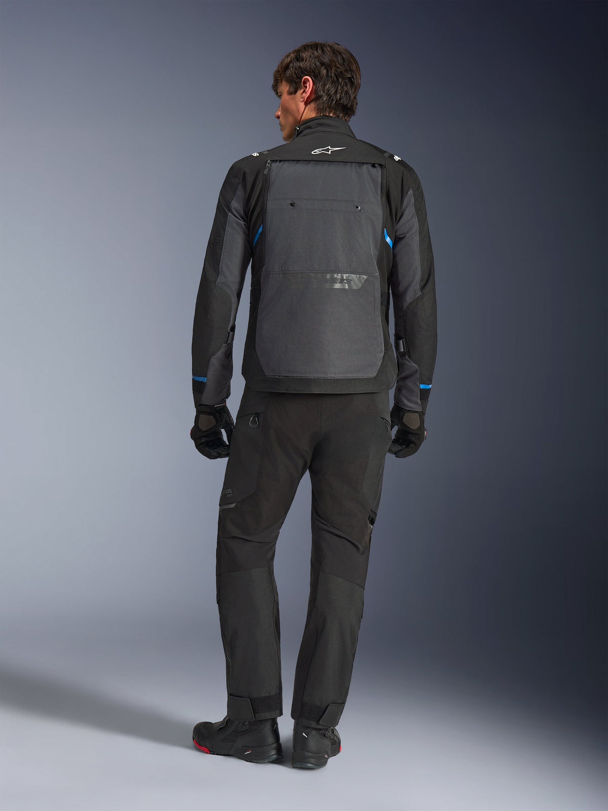 Alpinestars Cusco Drystar® Jacket, Black and Deep Gray with blue accents, rear view, worn with matching black adventure pants and gloves, featuring a large gray back panel and white logo on the collar, designed for road and adventure touring