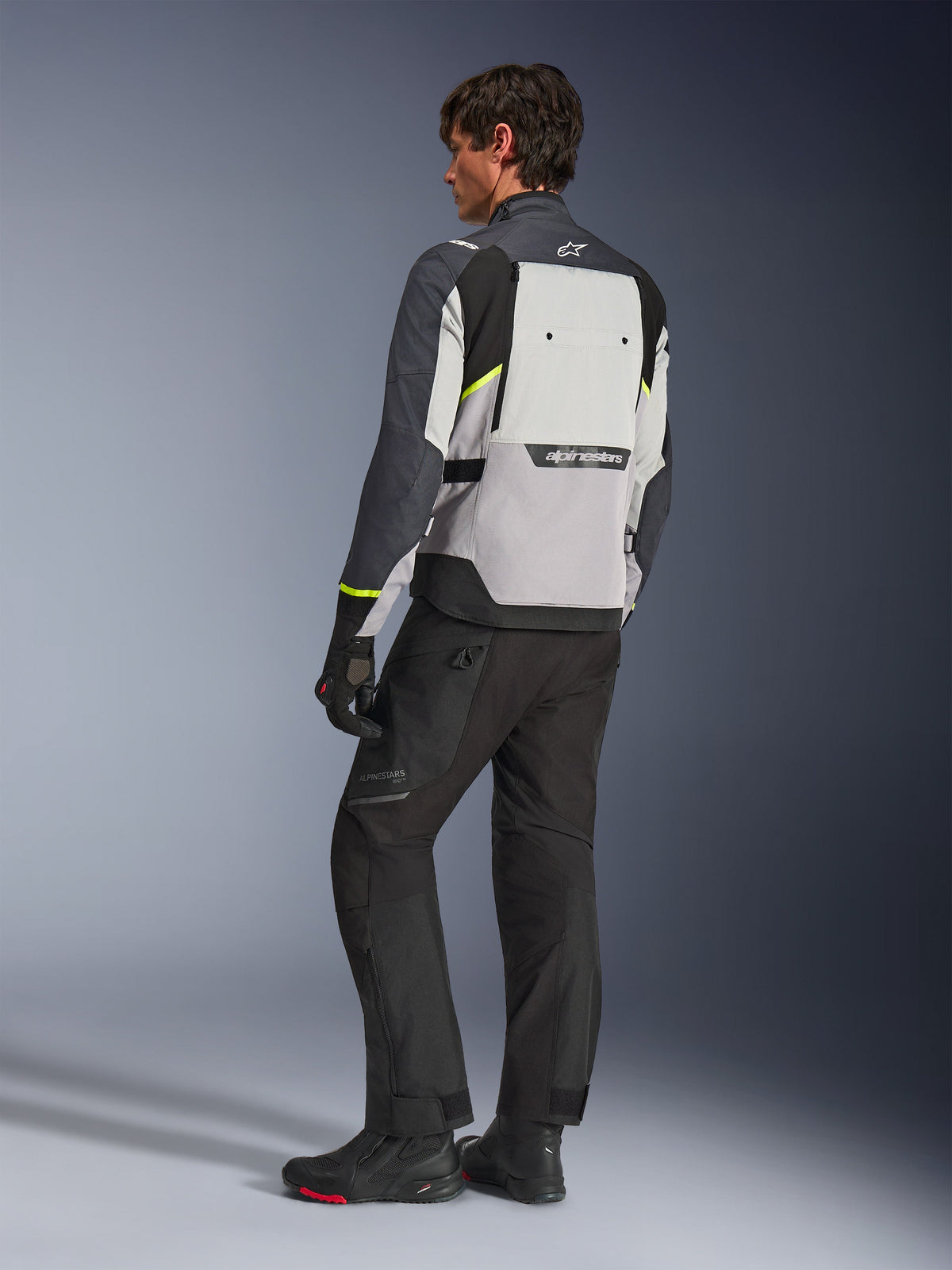 Alpinestars Cusco Drystar® Jacket in Ice Gray, Mid Gray, and Deep Gray, rear view on model, adventure touring jacket with neon yellow accents, worn with black riding pants and boots, featuring large back ventilation panel and Alpinestars branding.