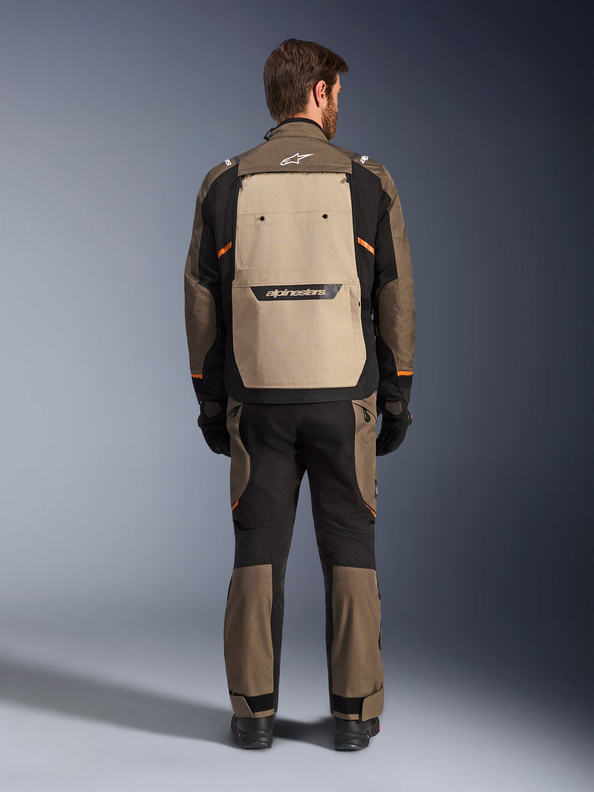 Alpinestars Cusco Drystar® jas, achteraanzicht, Walnut Aluminum Black, textiele adventure touring uitrusting, groot beige ventilatiepaneel op de rug met zwart logo, oranje accenten, gedragen met bijpassende broek en handschoenen