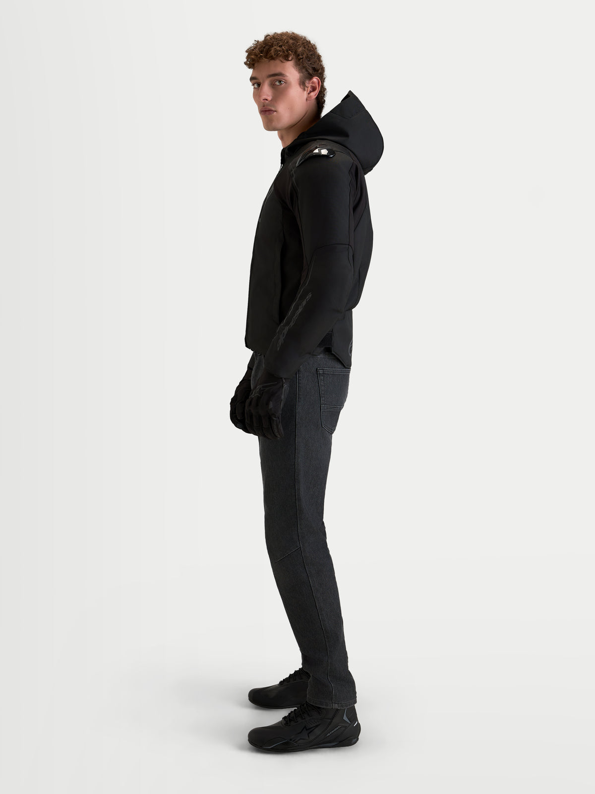 Veste imperméable Zaca V 2 d'Alpinestars, veste de moto sport textile noire avec capuche et protections d'épaules intégrées, portée par un modèle