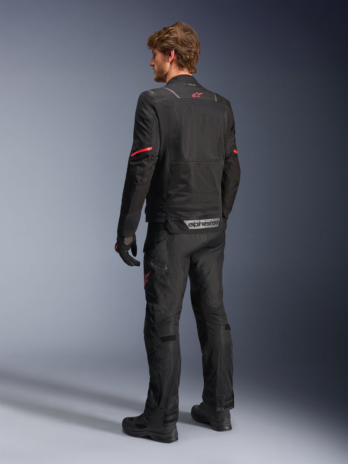 Alpinestars ST-2 Air Jas, zwarte adventure touring motorjas voor heren, achteraanzicht met mesh panelen, rood sterlogo en reflecterende details.