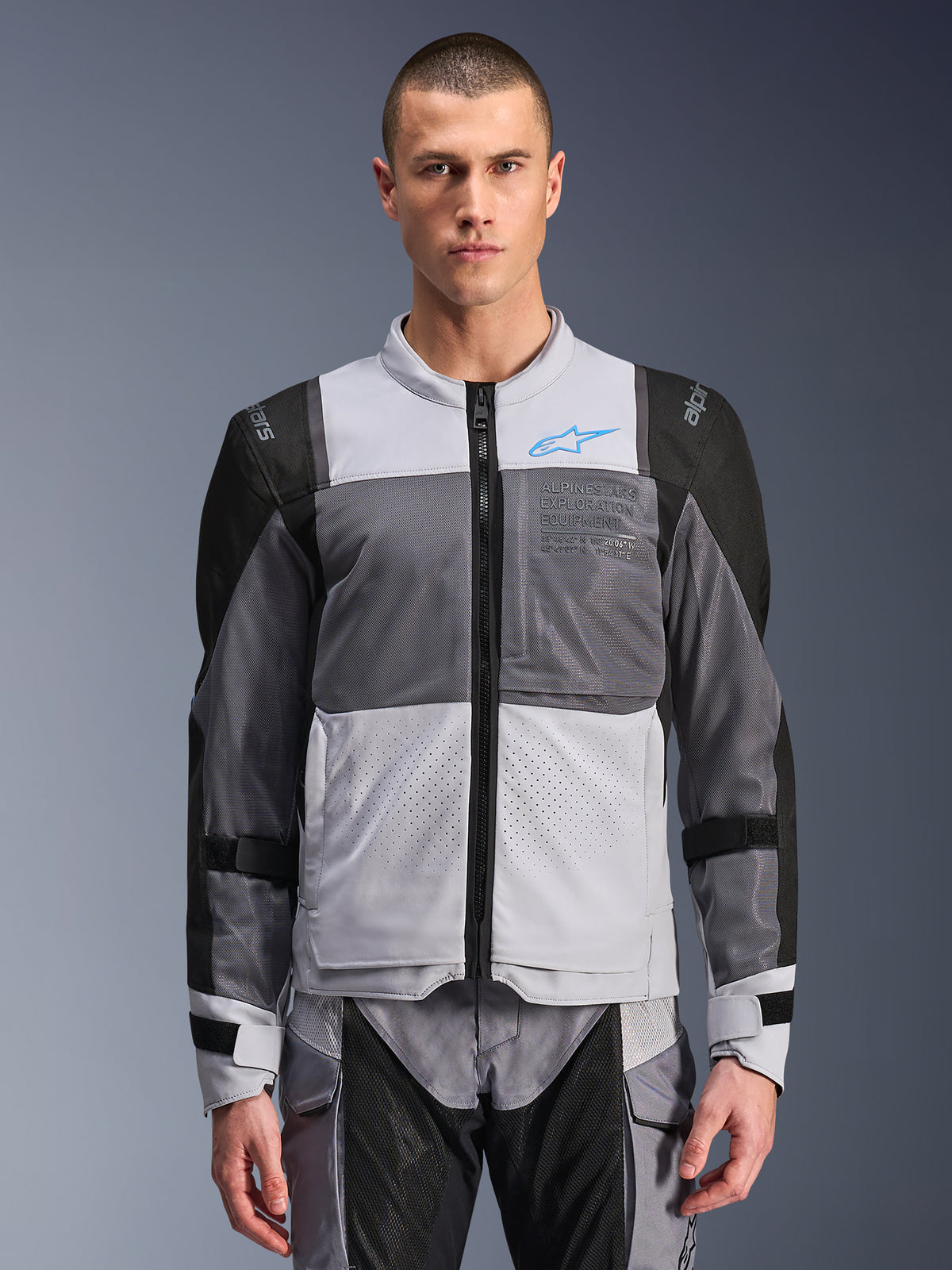 Alpinestars ST-2 Air Jacke, Motorradjacke für Herren, Eisgrau und Dunkelgrau mit schwarzen Akzenten, breite Mesh-Belüftungseinsätze, laserperforierte Vorderseite, blaues Alpinestars-Logo, Frontreißverschluss, getragen von einem Model mit passender Motorradhose