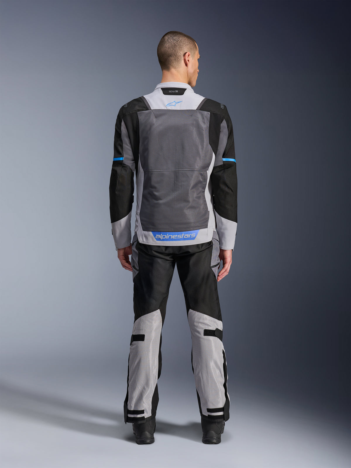 Alpinestars ST-2 Air Jacke, Ice Gray Dark Gray Black, Rückansicht am Modell, mit großen Mesh-Belüftungseinsätzen, blauen Akzenten und Alpinestars-Logo, kombiniert mit passender Motorradhose für Adventure-Touren.