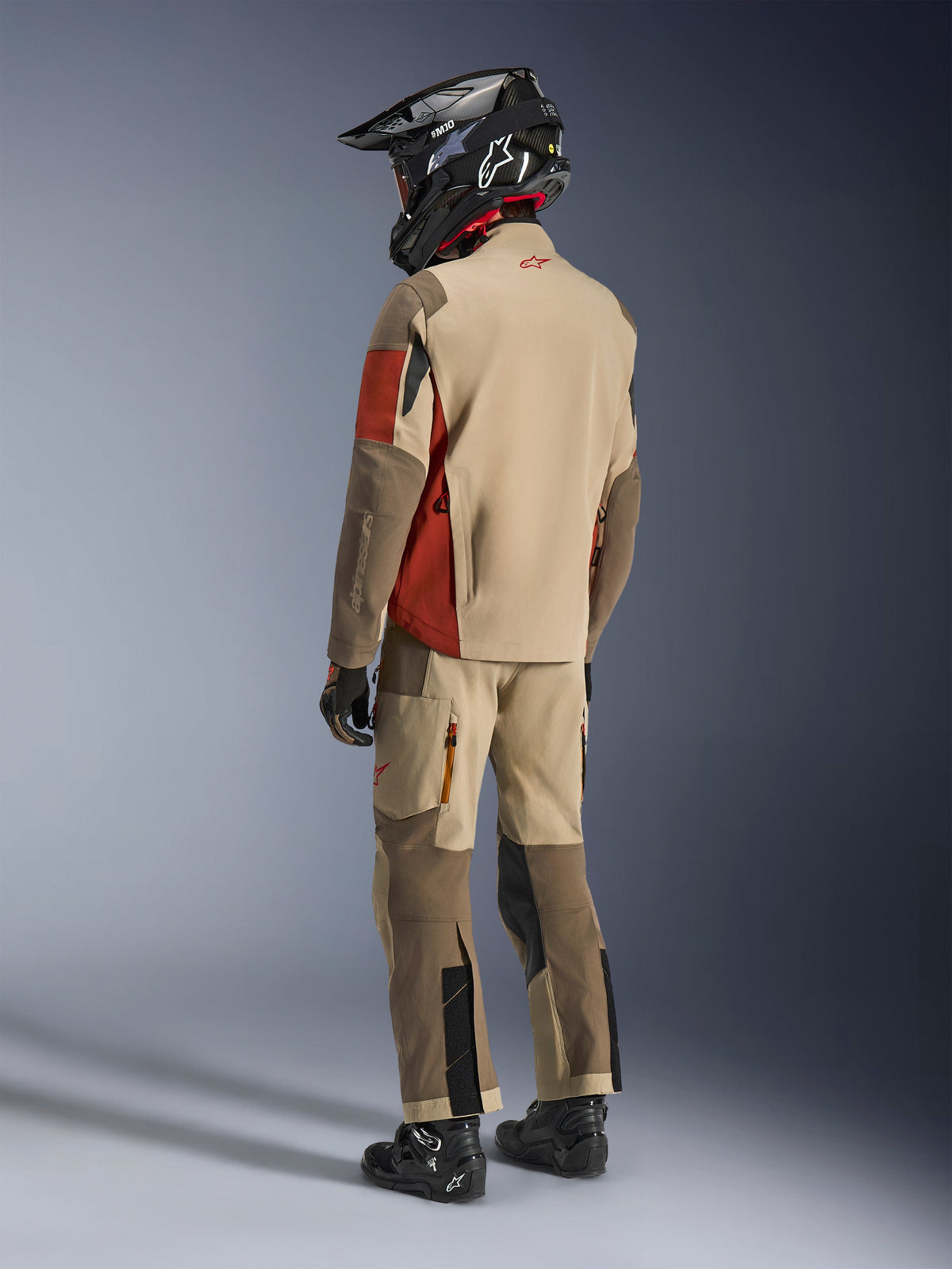 Adventure-Fahrer in der Rückansicht mit der Alpinestars Maxdura Drystar®XF Laminated Armored Shell in Aluminum Walnut Rust Brown, kombiniert mit passender Motorradhose, schwarzem Offroad-Helm und schwarzen Stiefeln, komplettes technisches Touren-Outfit.