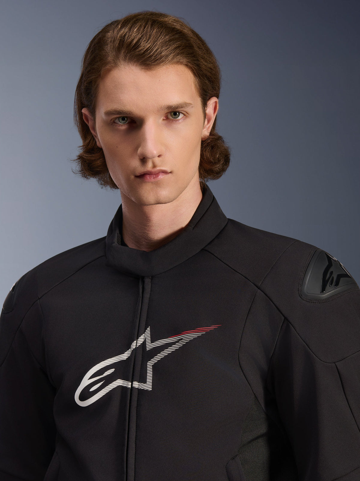 Model draagt de Alpinestars SMX Waterproof Jacket, zwart met witte en felrode accenten, voorzien van een groot wit sterlogo met een rode streep op de borst, DFS Lite-schouderbeschermers en een gestroomlijnde textielconstructie voor motorprestaties op de weg.