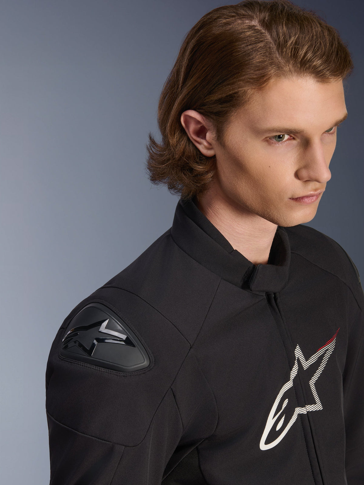 Alpinestars SMX Waterproof Jacket, zwart met witte en rode accenten, close-up lifestylefoto van een mannelijk model, met externe DFS Lite schouder sliders en groot sterlogo op de borst, sportieve motorkleding