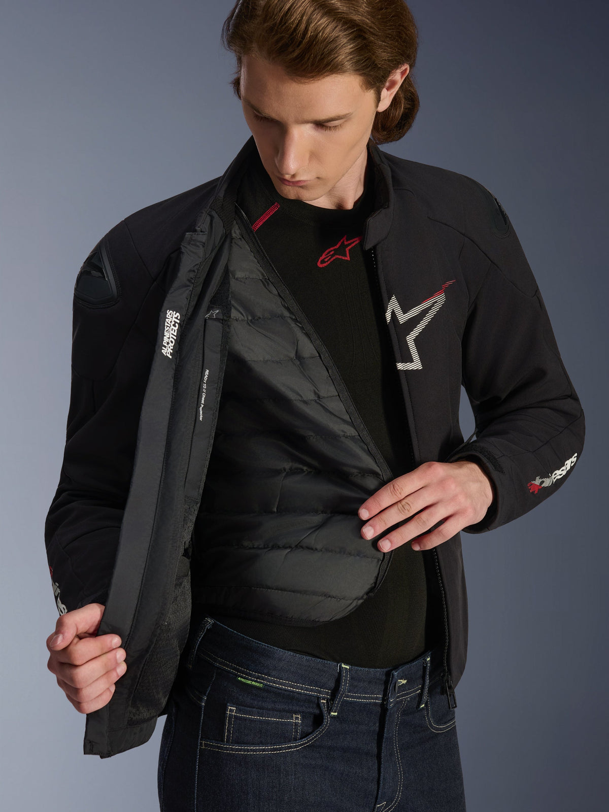 Alpinestars SMX Waterdichte Jas in zwart, wit en felrood, gedragen door een man en opengeritst om de gewatteerde uitneembare thermische voering te tonen, voorzien van externe DFS Lite-schouders en witte logodetails, hoogwaardige motorkleding voor op de weg