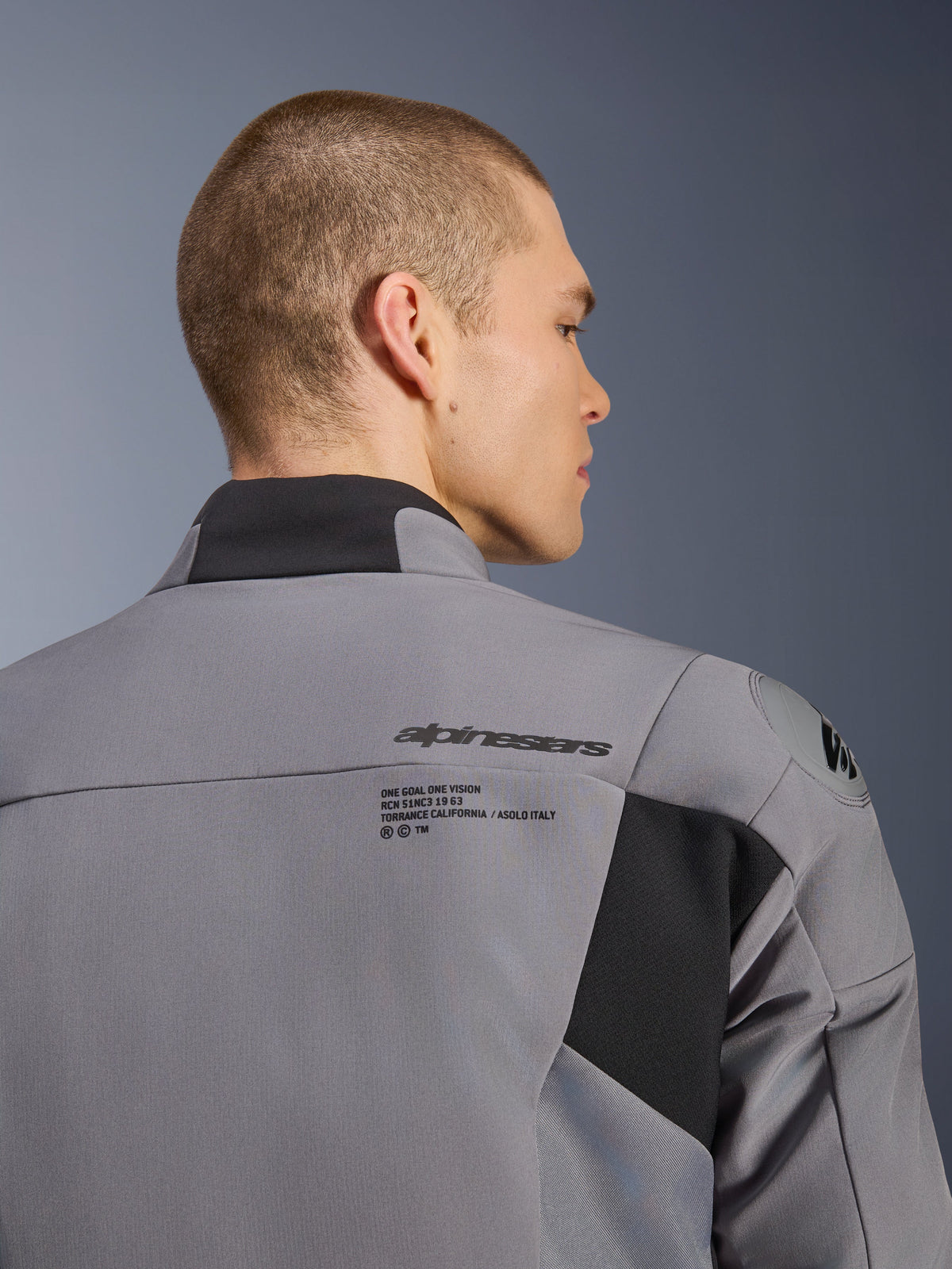 Alpinestars SMX Waterproof Jacket in donkergrijs zwart, close-up van de rug en schouder met Alpinestars branding en DFS lite schouderbescherming, gedragen door een mannelijk model