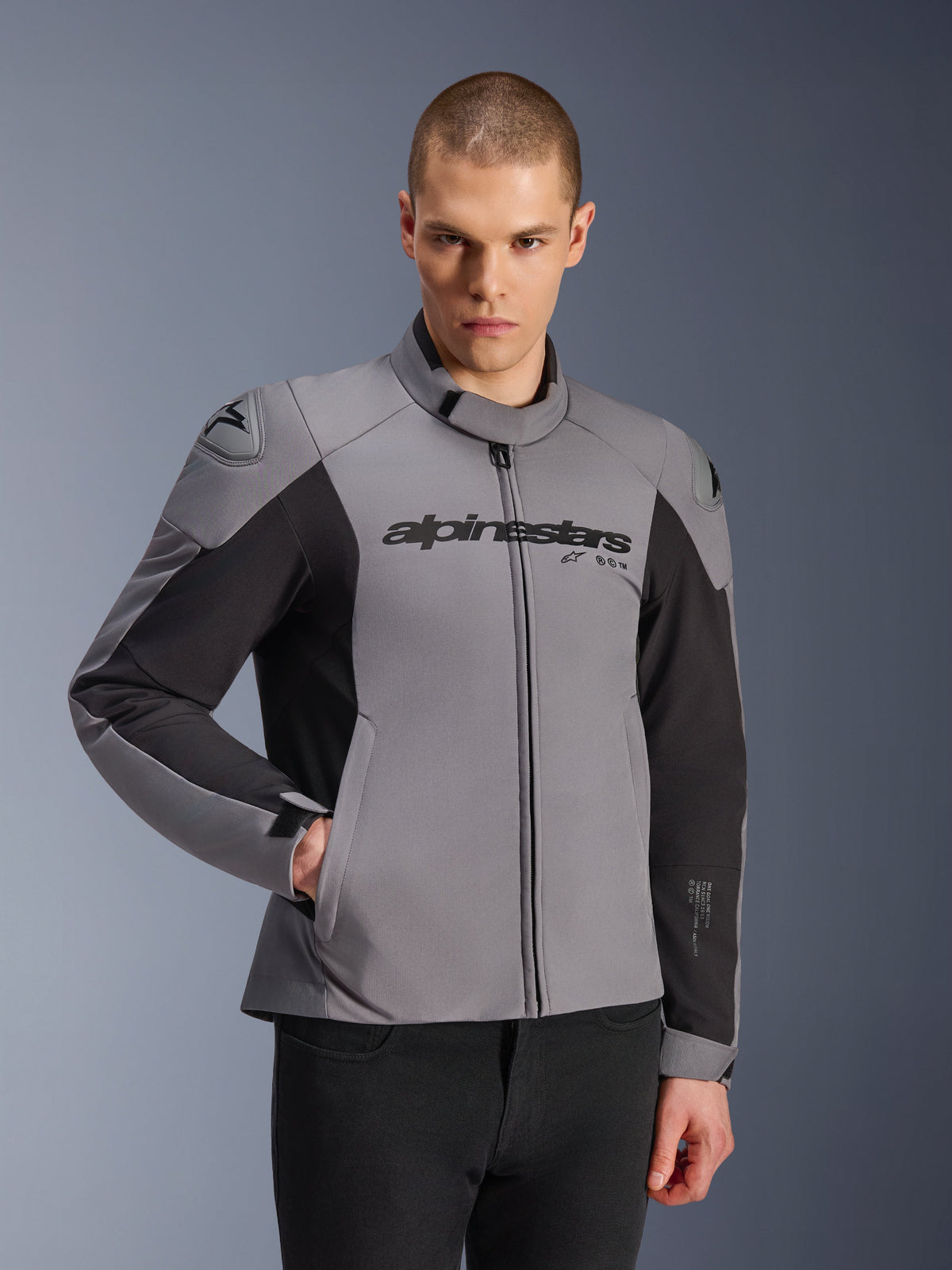 Alpinestars SMX Waterproof Jas, donkergrijs en zwart, gedragen door een mannelijk model, voorzien van 'alpinestars' logo op de borst, DFS Lite schouderbescherming, strak sportief design met textiel en softshell materialen voor rijden op de weg.