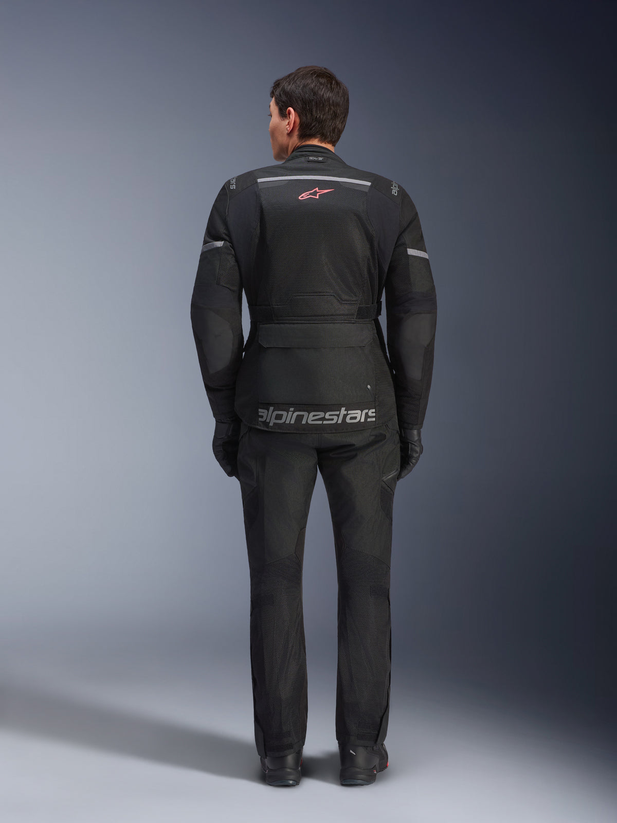 Rear view of a rider wearing the Alpinestars Andes Air Drystar® Jacket in Black, featuring extensive mesh ventilation panels on the back, red Alpinestars logo, and reflective accents, paired with matching motorcycle pants and gloves for adventure touring.