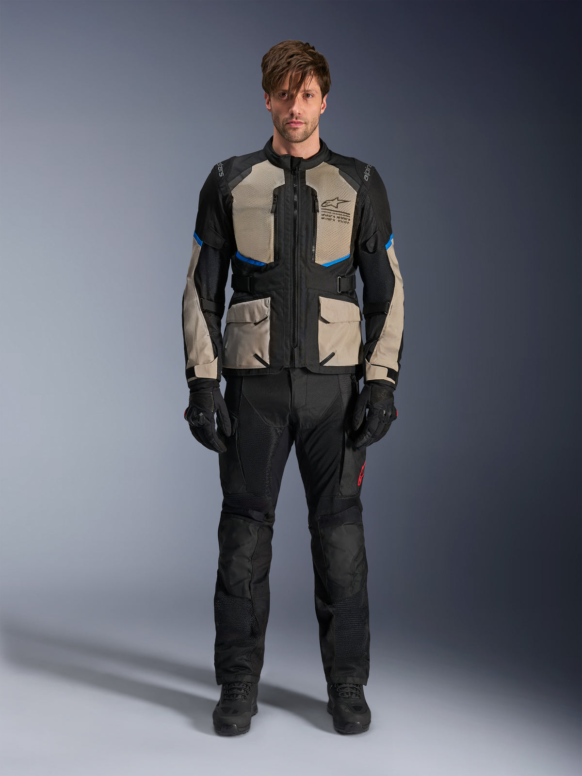 Model draagt Alpinestars Andes Air Drystar® jas, motor touringjas, Black Laurel Gray en Bright Blue, gecombineerd met bijpassende zwarte rijbroek en handschoenen, voorzien van uitgebreide mesh ventilatiepanelen op de borst en mouwen voor adventure touring in warm weer.