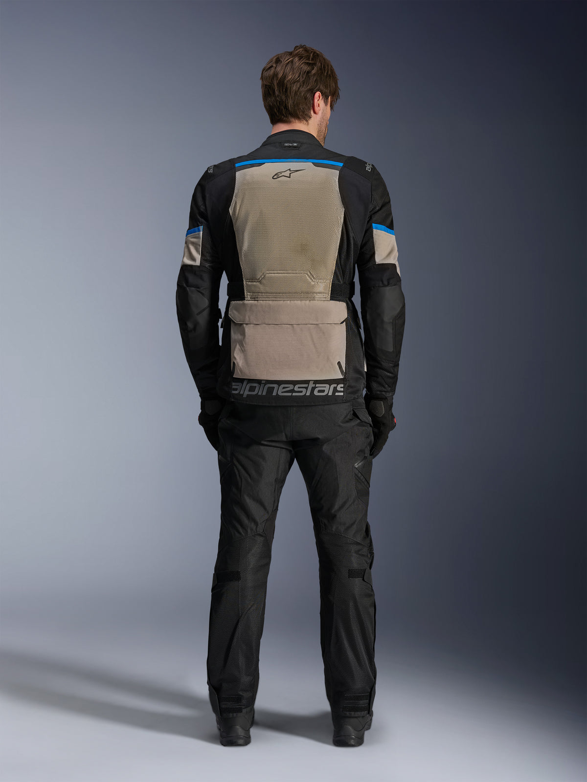 Alpinestars Andes Air Drystar® Jas, Black Laurel Gray Bright Blue, achteraanzicht met een uitgebreid mesh ventilatiepaneel, grote opbergzak op de onderrug met Alpinestars-branding, technische motor touringjas gedragen met bijpassende broek.