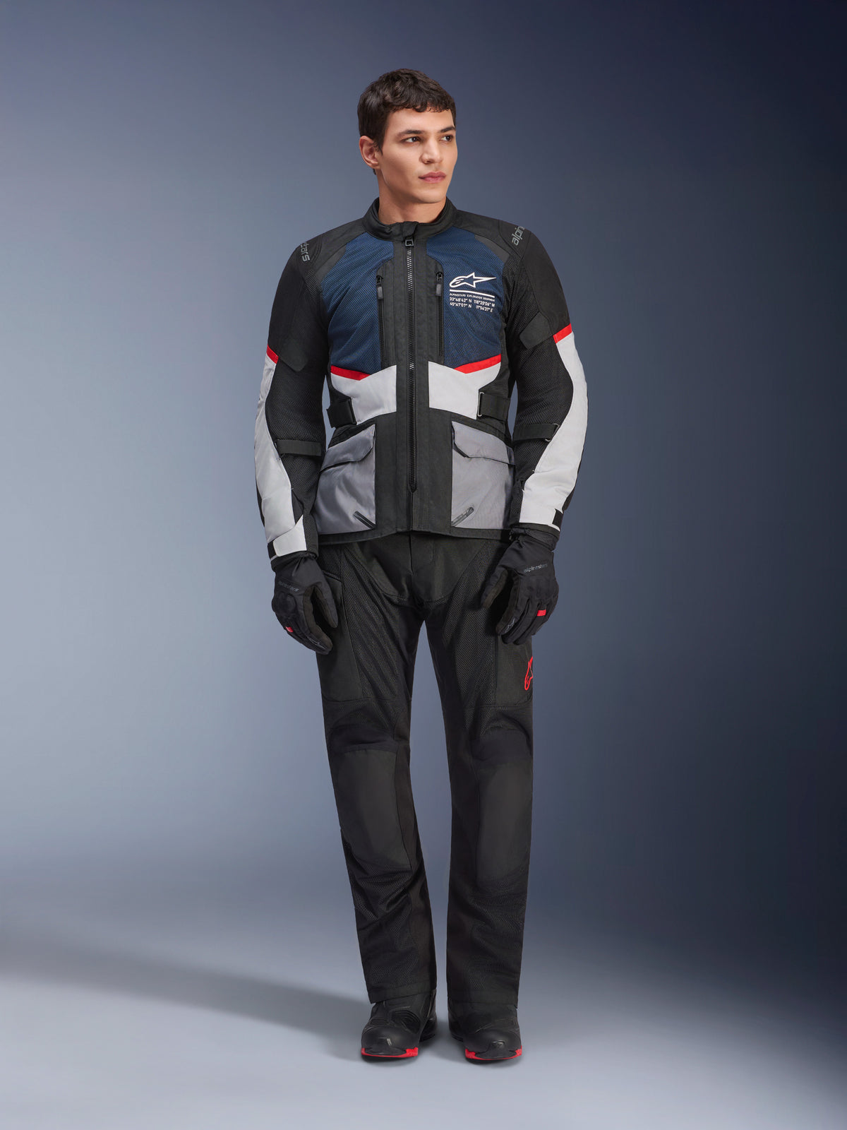Alpinestars Andes Air Drystar® Jas, motortouringjas, Deep Blue Black en Ice Gray, gedragen met bijpassende zwarte adventure-broek en handschoenen, voorzien van mesh-panelen voor luchtstroom en een technisch ontwerp met meerdere zakken.