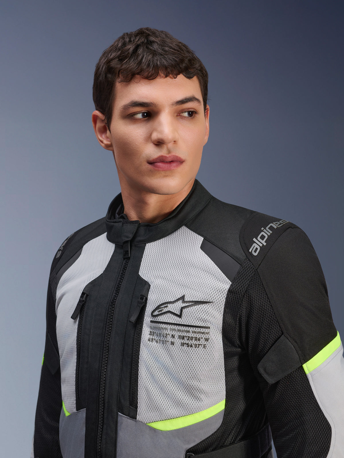 Veste Alpinestars Andes Air Drystar®, veste de moto touring, gris glacé et gris foncé avec des touches jaune fluo, portée par un mannequin homme, dotée de panneaux en maille 2D pour la ventilation, logo Alpinestars avec coordonnées sur la poitrine et construction textile durable.