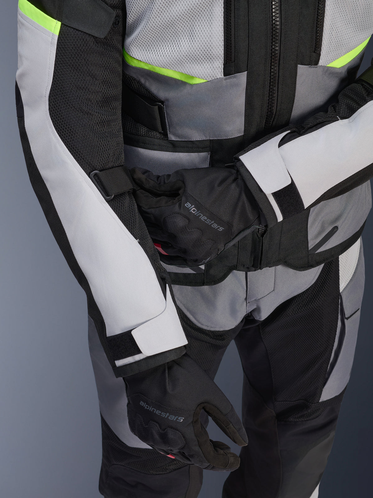 Veste Alpinestars Andes Air Drystar®, veste de touring moto, gris glace et gris foncé avec des accents jaune fluo, gros-plan montrant les panneaux en mesh et les sangles de réglage, portée avec des gants Alpinestars noirs