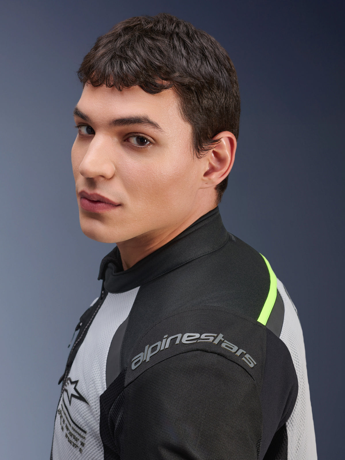 Gros plan d'un mannequin portant la veste Alpinestars Andes Air Drystar® en gris glace, gris foncé et noir, avec des accents jaune néon et des panneaux en mesh, le logo Alpinestars étant visible sur l'épaule.