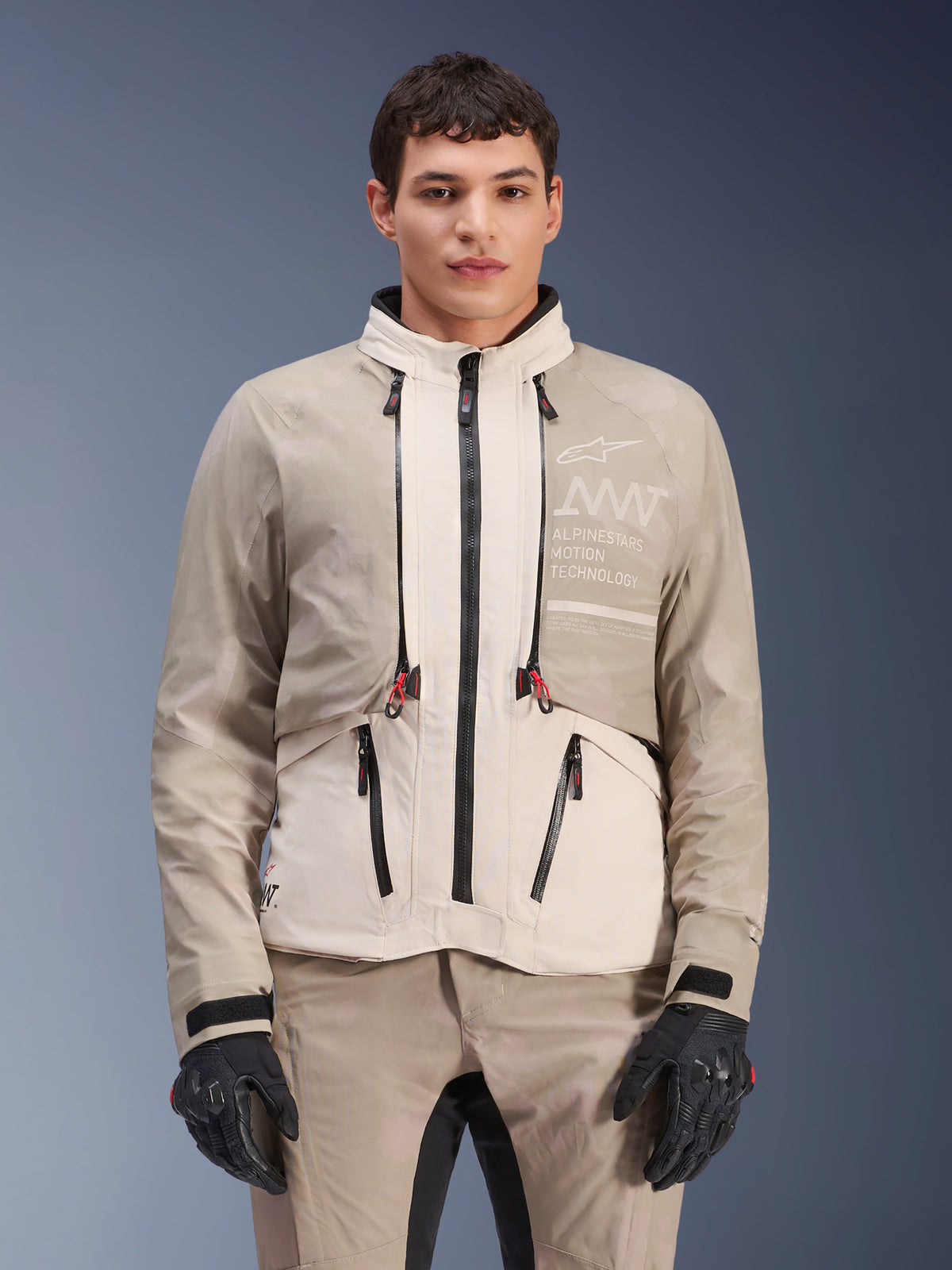 Alpinestars AMT-10LAB Drystar® XF Jacke, Adventure-Motorradjacke, White Sand Aluminum Camo, modulares Design mit schwarzen Reißverschlüssen und roten Akzenten, kombiniert mit passender Hose und schwarzen Handschuhen, Alpinestars Motion Technology Branding auf der Brust, professioneller Allwetter-Motorradanzug