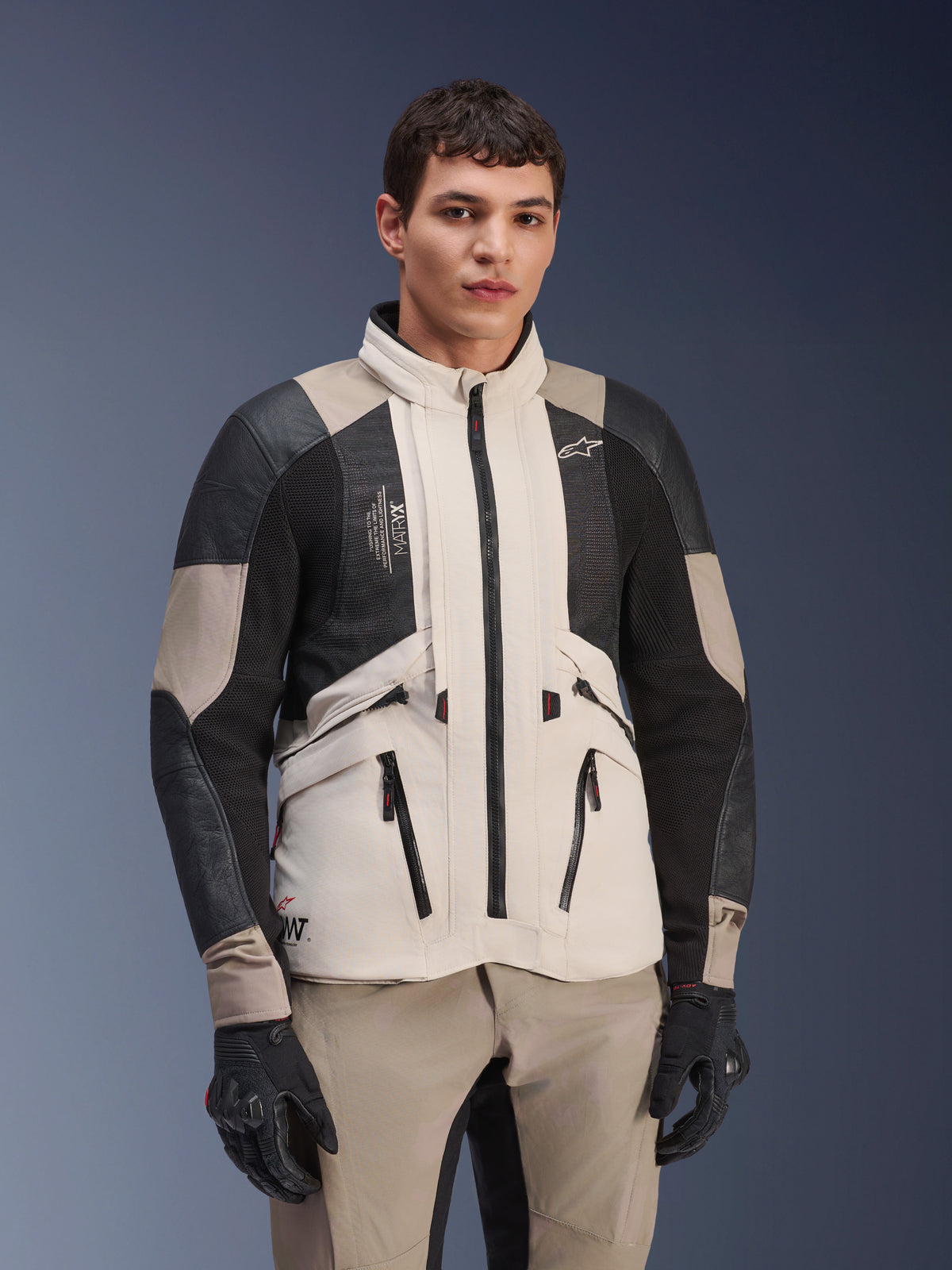 Alpinestars AMT-10LAB Drystar® XF Jacke, White Sand Aluminum Camo, Motorrad-Adventure-Jacke mit schwarzen MATRYX® Mesh-Einsätzen und Lederverstärkungen, getragen von einem Modell mit schwarzen Handschuhen und passender sandfarbener Hose, Studioporträt