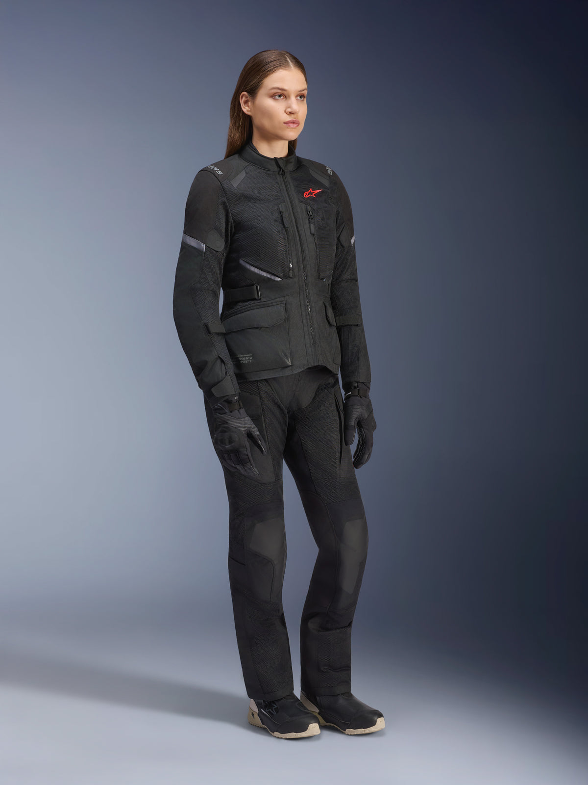 Femme portant la veste Alpinestars Stella Andes Air Drystar®, veste de touring aventure en textile noir, avec pantalon et gants noirs assortis, dotée de larges panneaux de ventilation en maille et d'un logo rouge, tenue de moto coordonnée pour femme